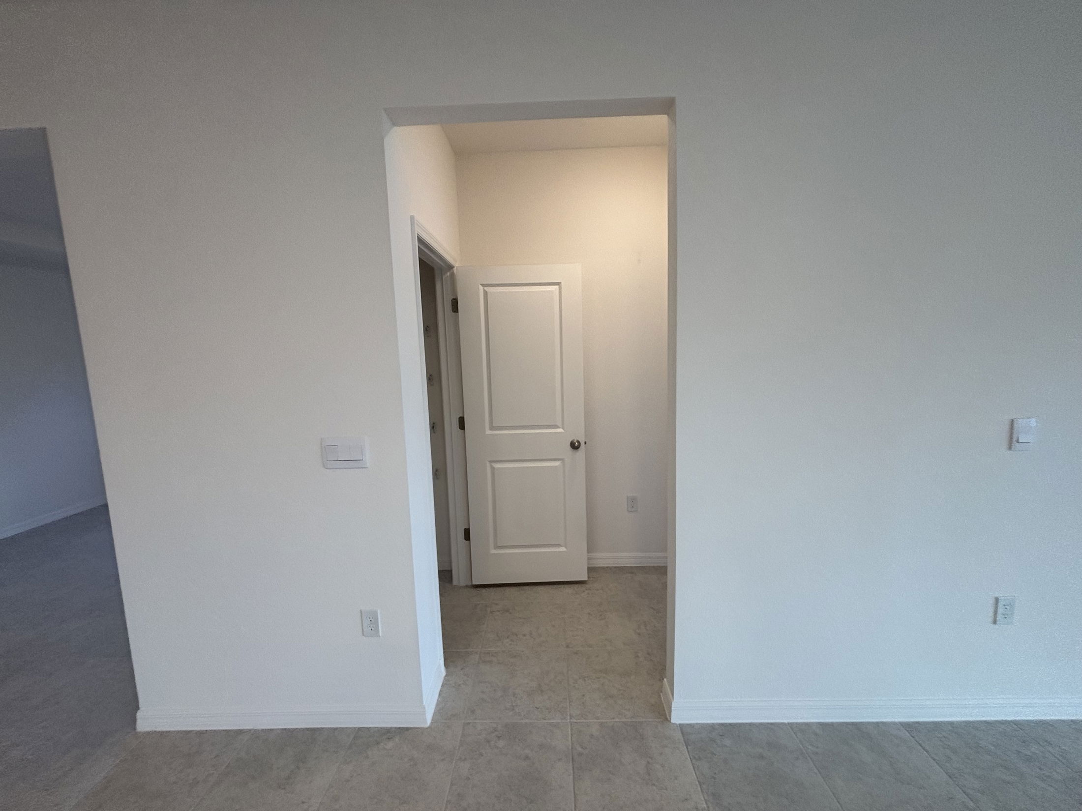 Interior view of a modern home featuring a doorway leading to a room with light-colored walls and tiled flooring.