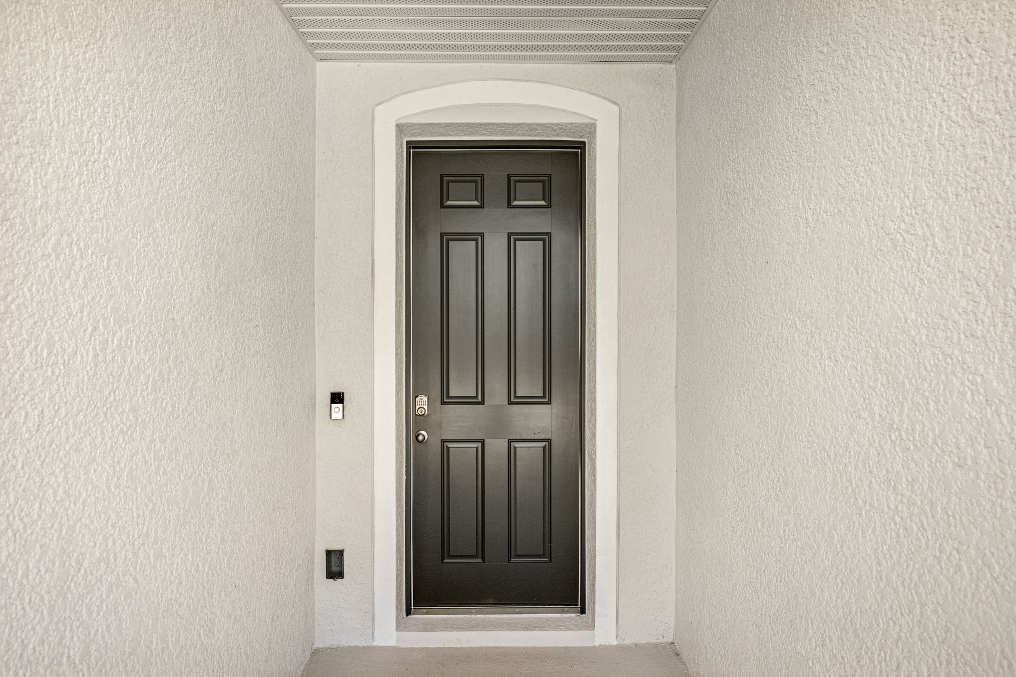 A modern black front door with a keypad lock and surrounding white walls in a welcoming entryway.