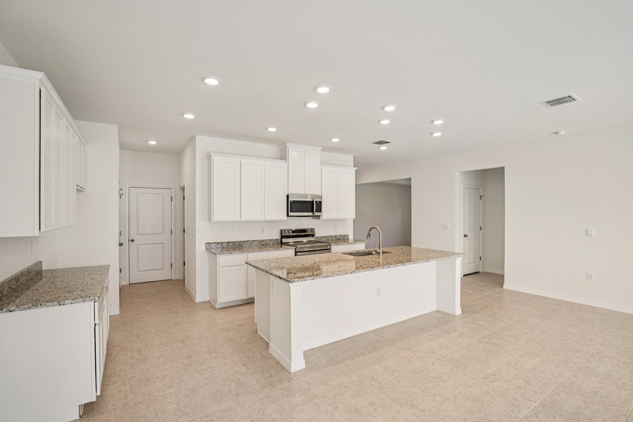 Modern kitchen interior featuring granite countertops, sleek white cabinetry, and stainless steel appliances in a bright open layout.