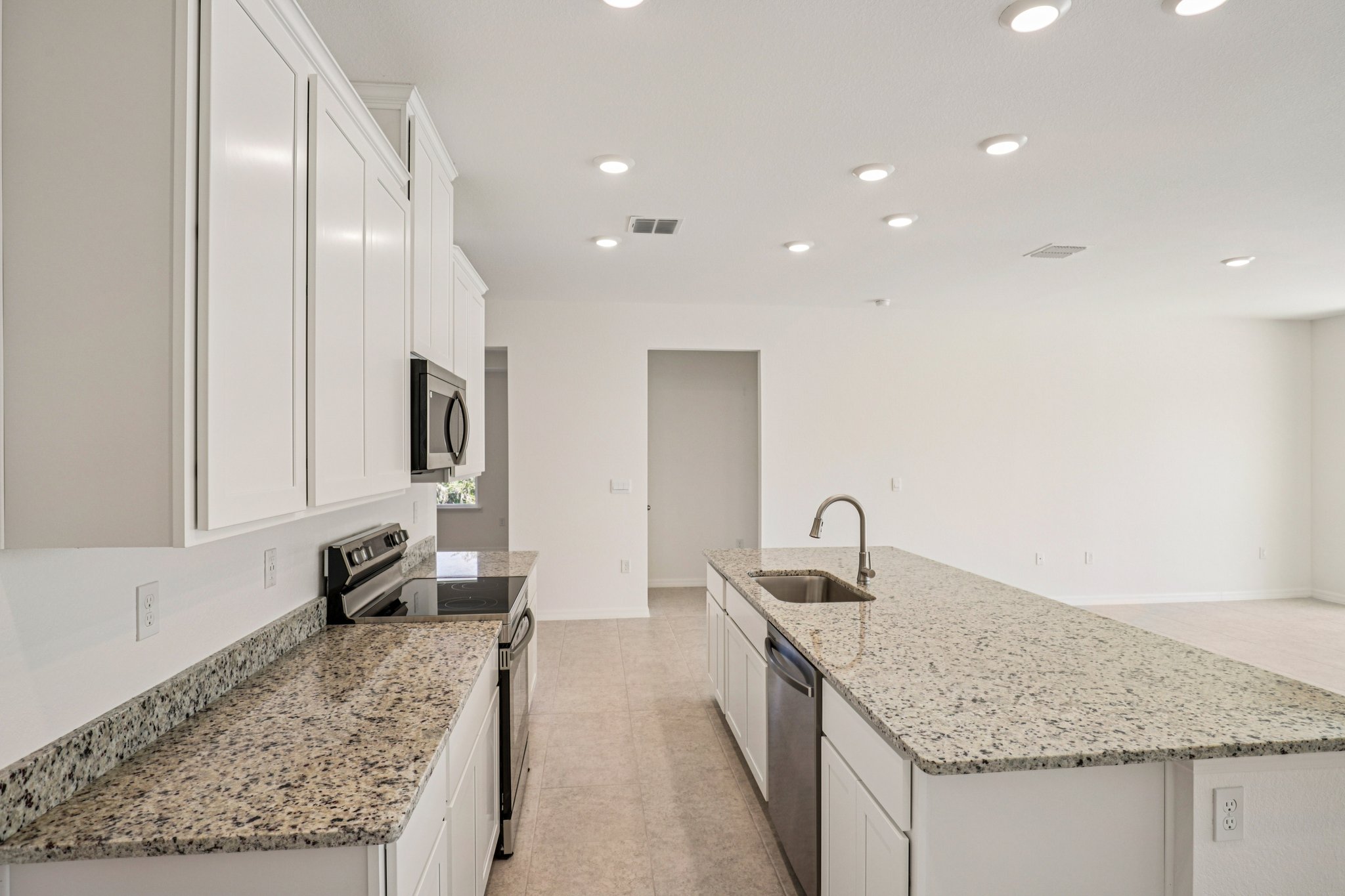 Modern kitchen featuring white cabinets, granite countertops, stainless steel appliances, and recessed lighting in a spacious open layout.