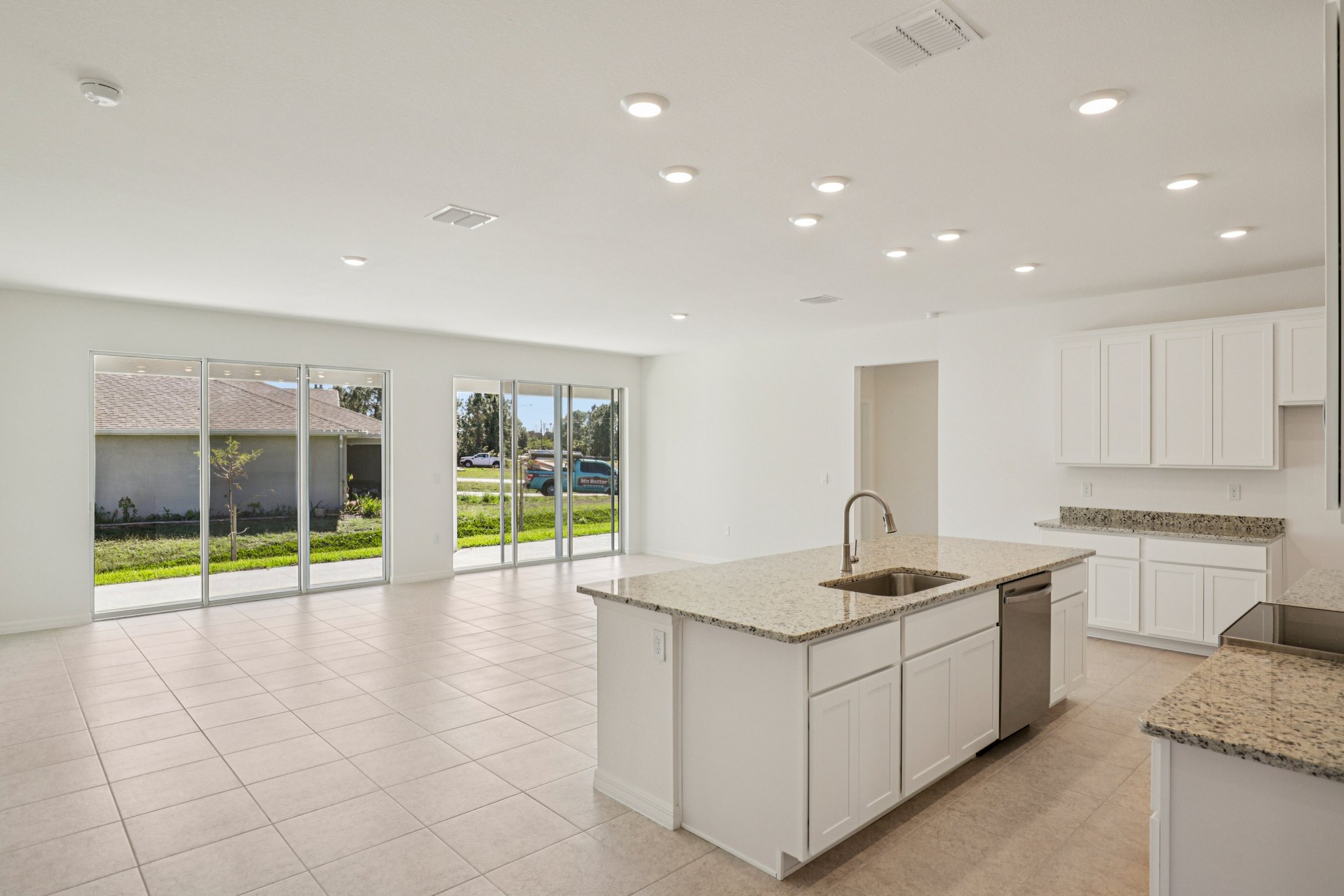 Modern open-concept kitchen featuring a large granite island, white cabinetry, and sliding glass doors that lead to a bright outdoor space.