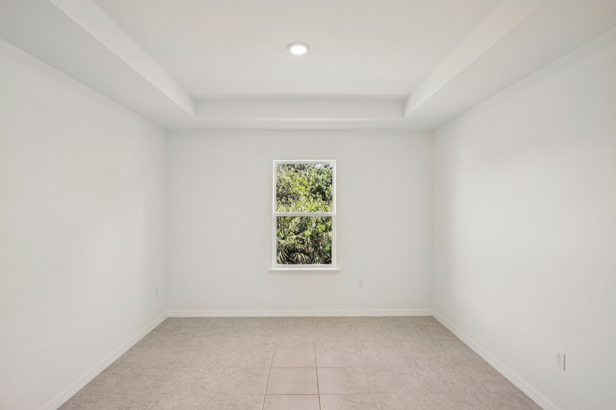 Bright and spacious empty room with white walls and a window overlooking lush greenery.