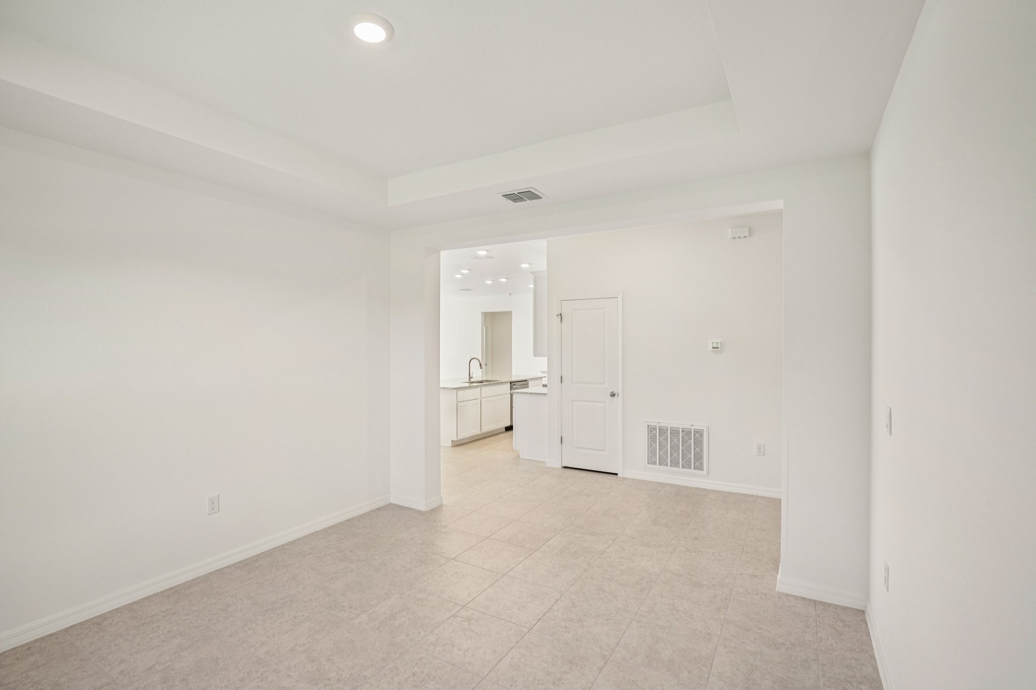 Modern open-concept living room with tile flooring and a view into a bright, contemporary kitchen.
