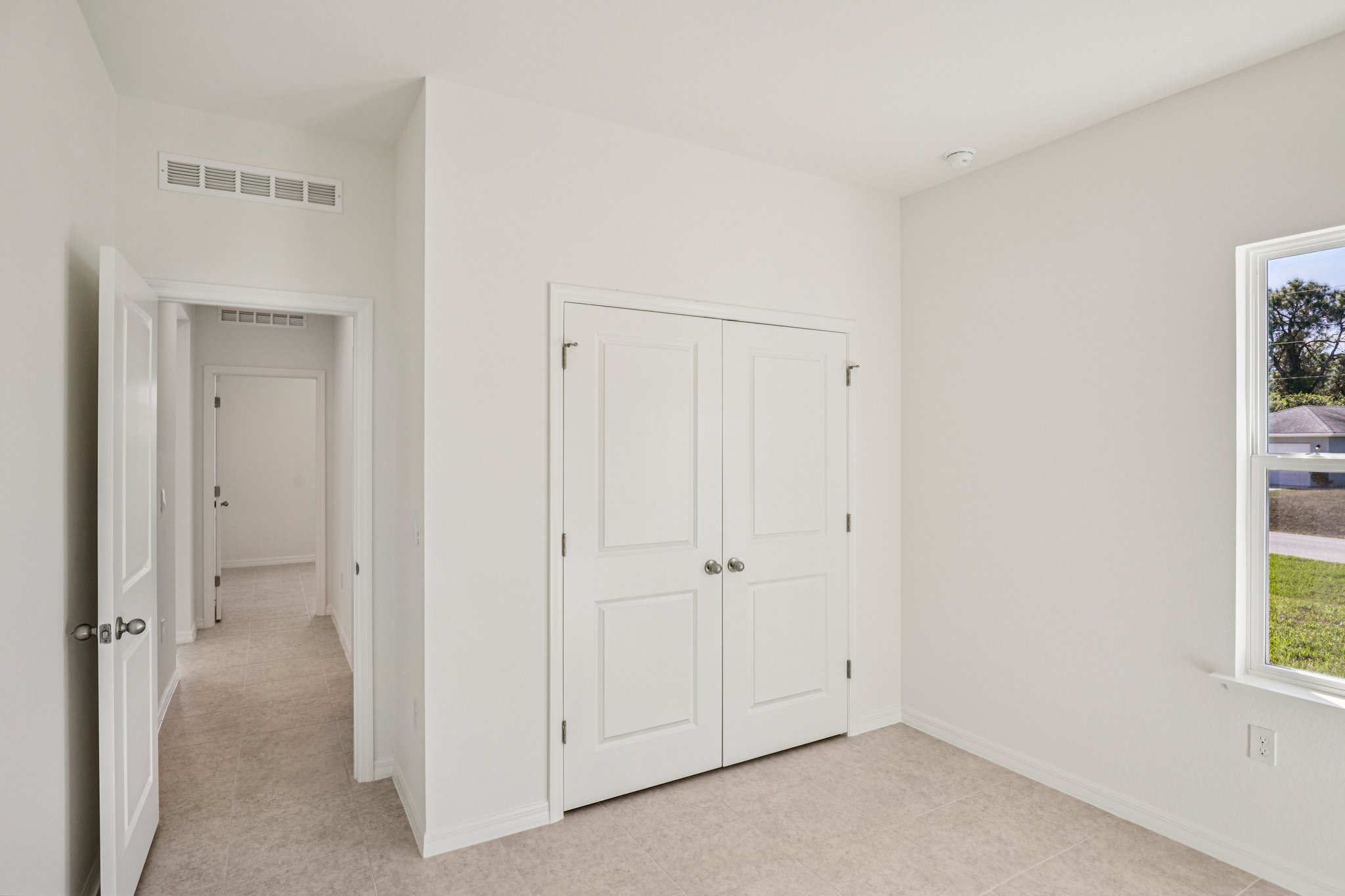 Bright and spacious bedroom interior with white walls, double closet doors, and natural light from a large window.