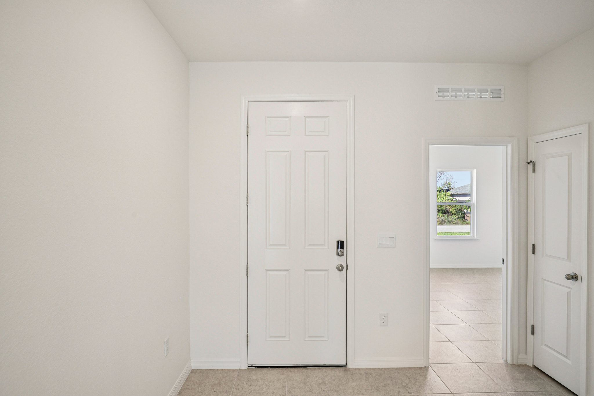 Modern white entryway with a front door and adjacent room showcasing large windows and tiled flooring.