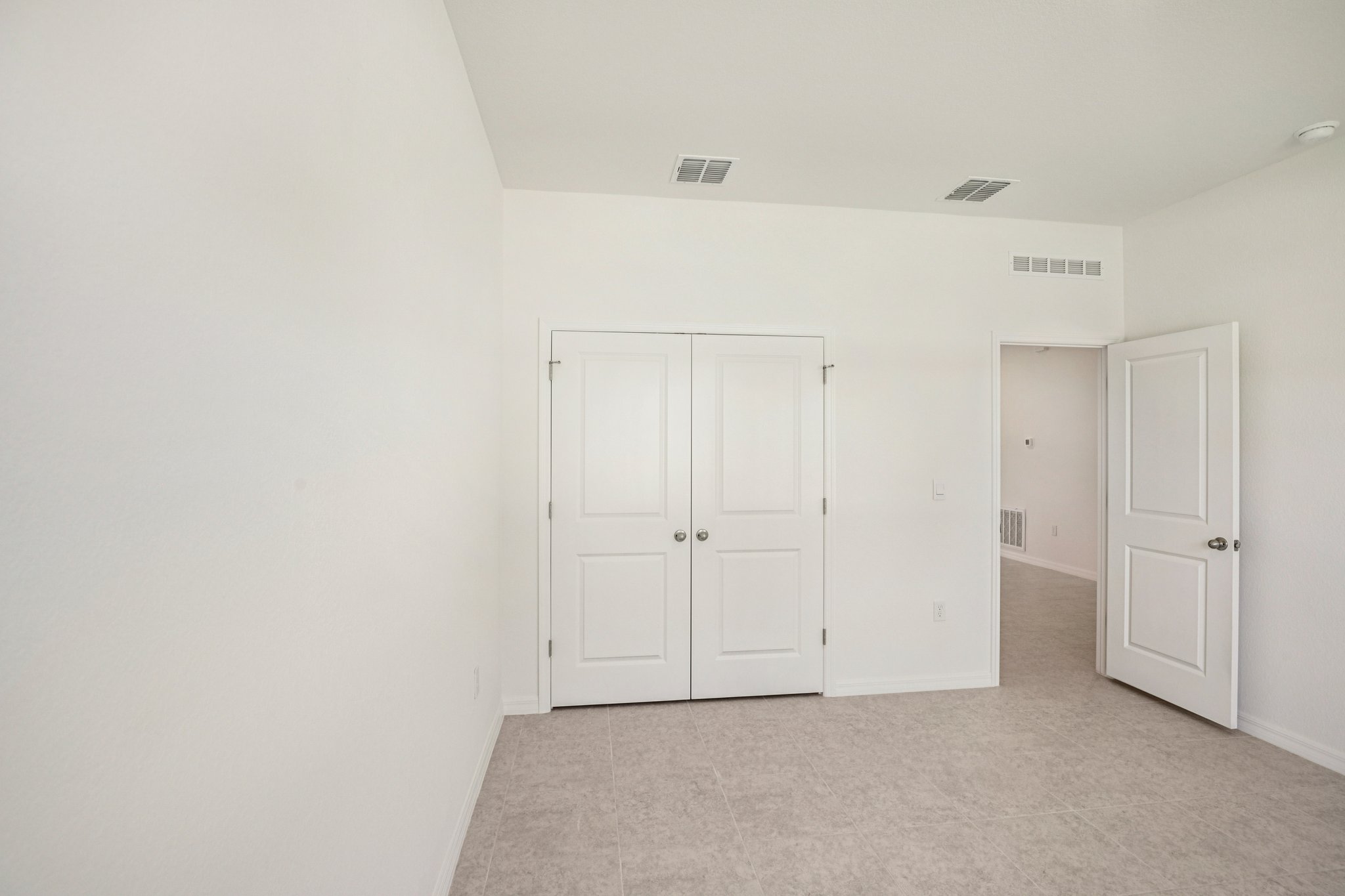 Bright and spacious interior of a modern room featuring double white doors and neutral tile flooring.