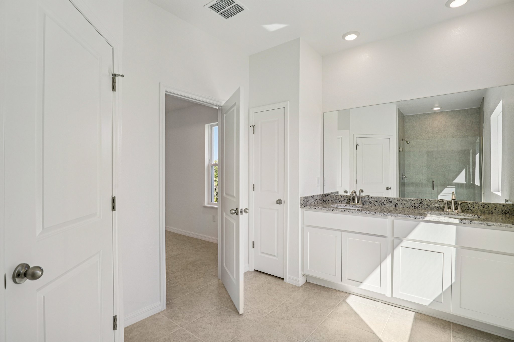 Spacious modern bathroom featuring a double sink vanity, granite countertops, and a glass shower in natural light.