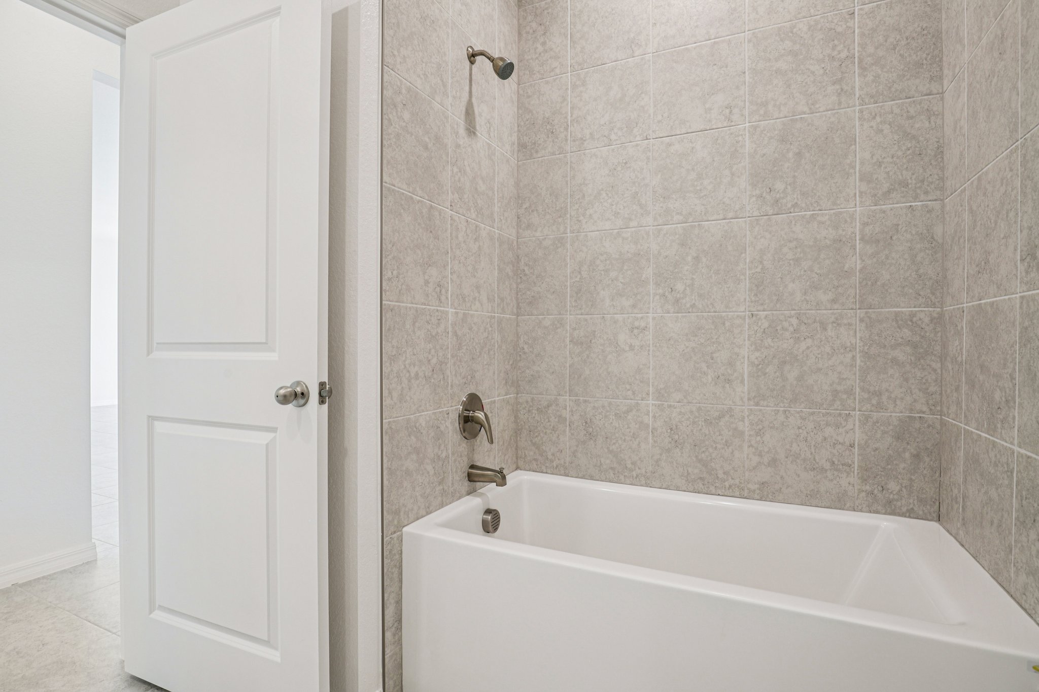 Modern bathroom featuring a white bathtub with a showerhead and gray tiled walls.