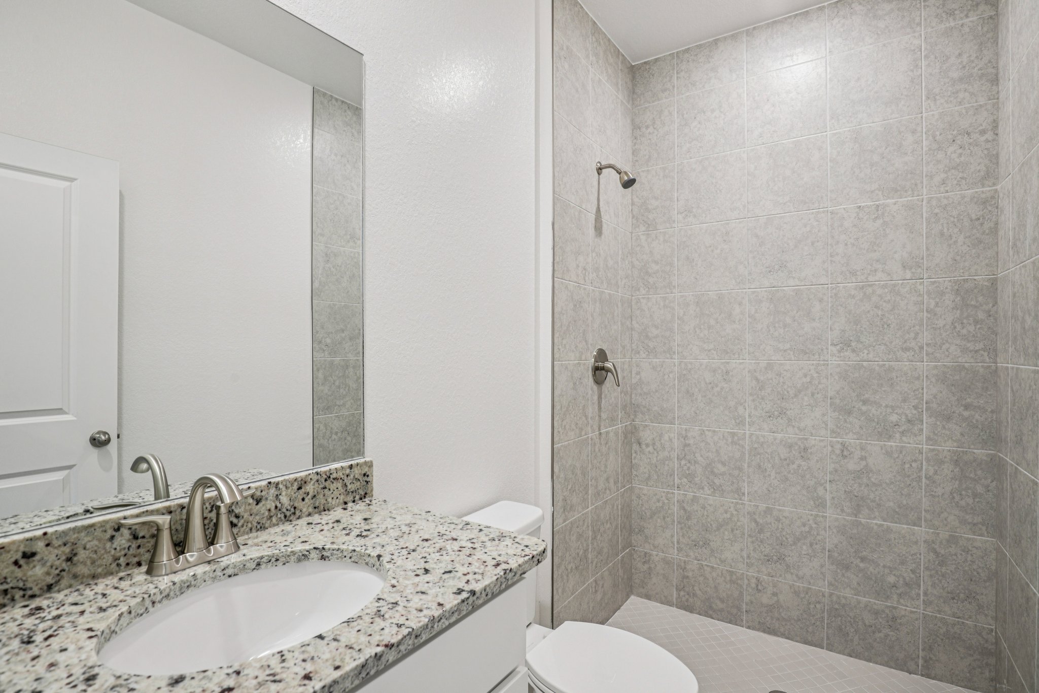 Modern bathroom featuring granite countertop, mirror, and tiled shower enclosure.