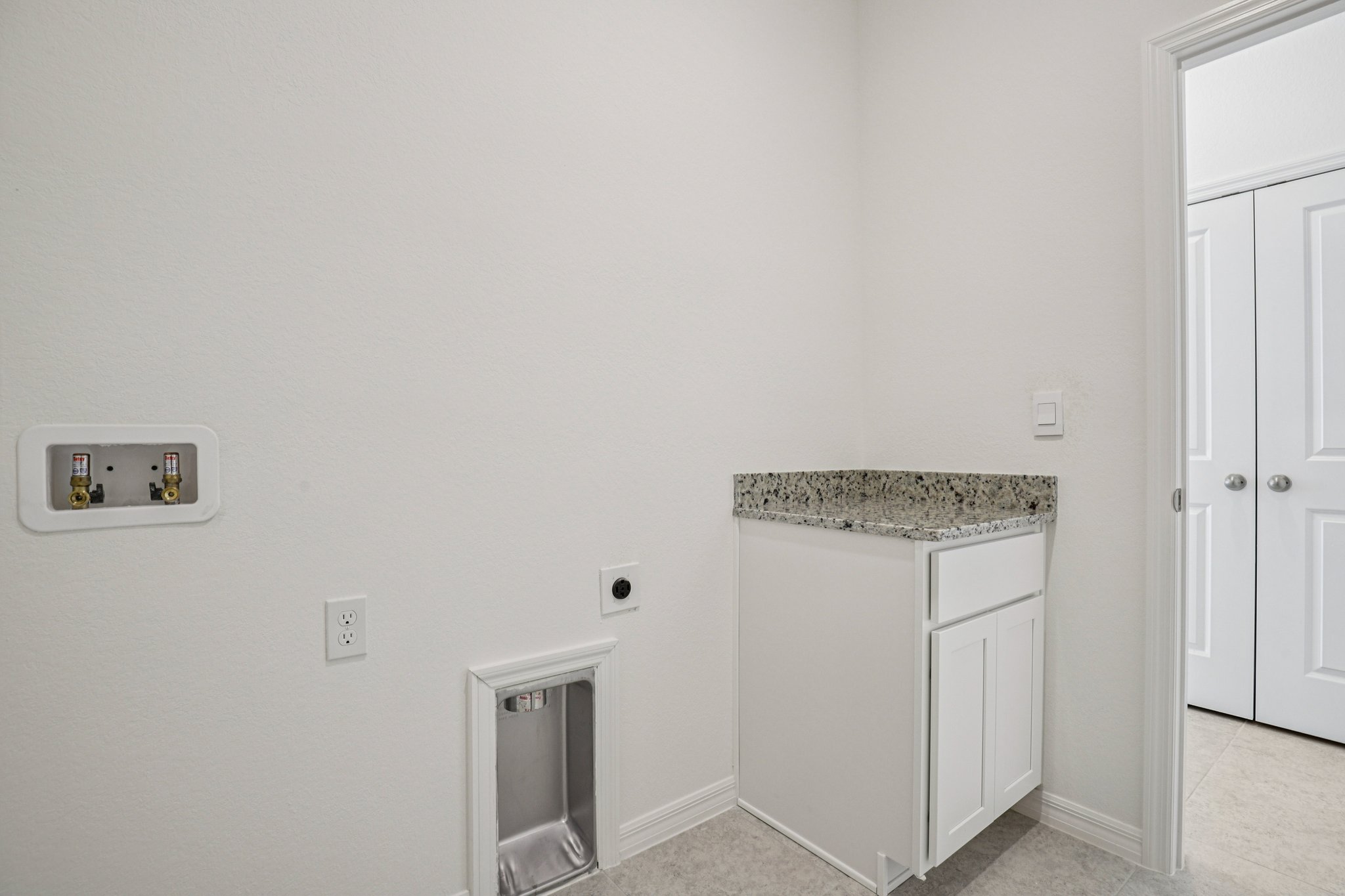 Modern laundry room with granite countertop, white cabinetry, and minimalistic design.
