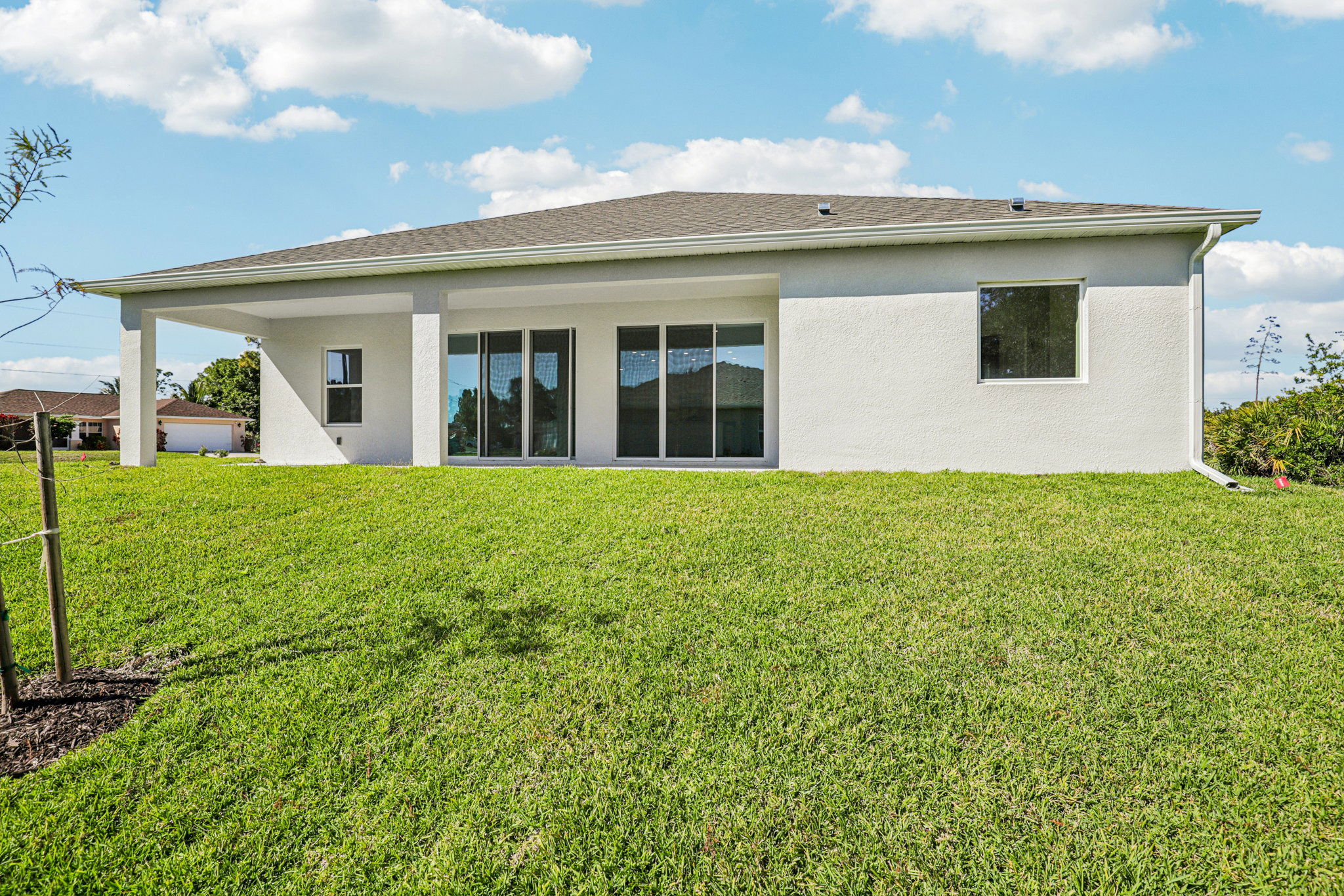 A modern single-story house with large windows and a well-maintained grassy yard under a blue sky.