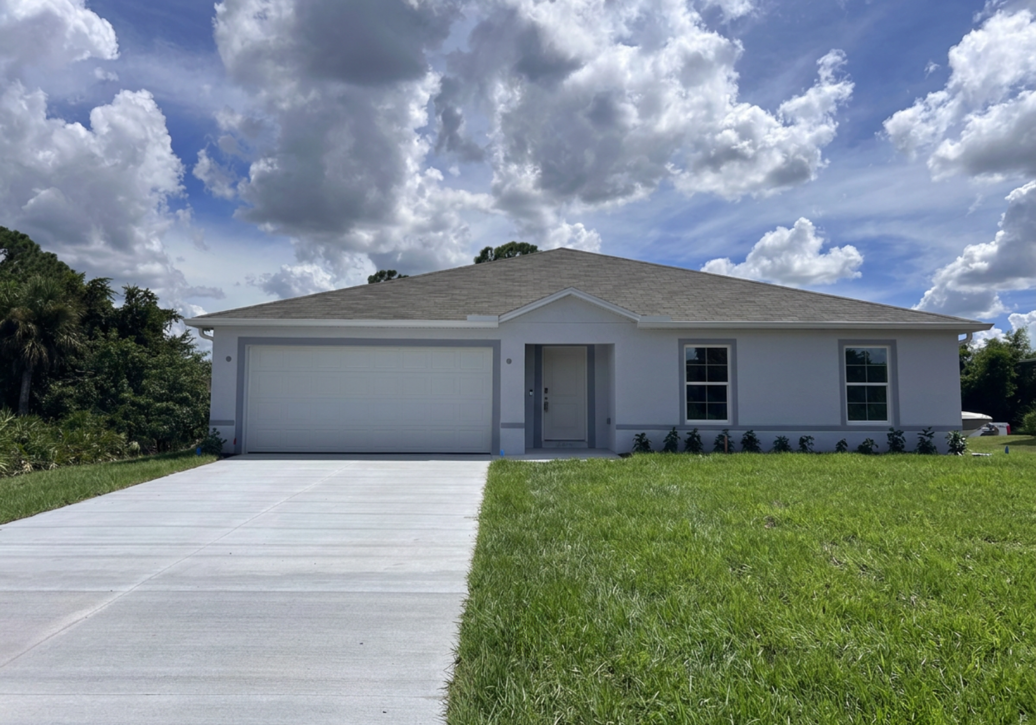 A single-story house with a garage, set on a grassy lawn under a cloudy blue sky.