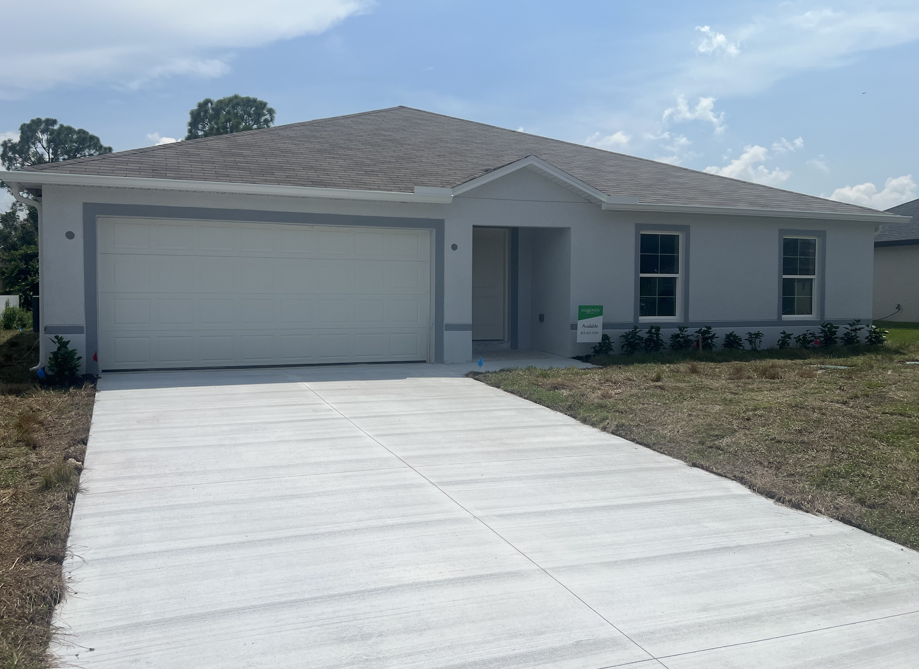Single-story residential home with a gray exterior, two front windows, and a garage, surrounded by a lawn.