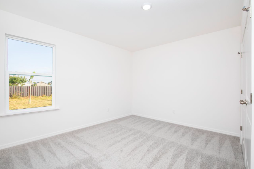 Empty room with white walls, natural light from a window, and light gray carpet flooring.