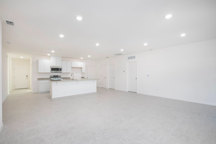 Modern open-concept kitchen and living area with granite countertops and neutral tile flooring.