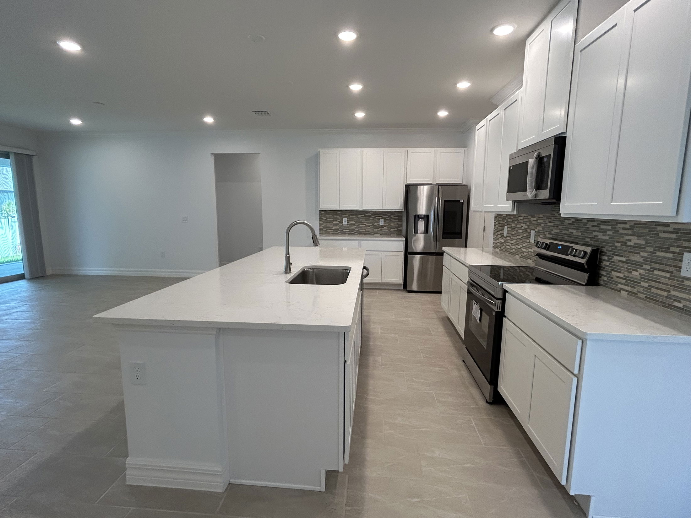 Modern kitchen with white cabinets, stainless steel appliances, and a large island with a sink and quartz countertops.