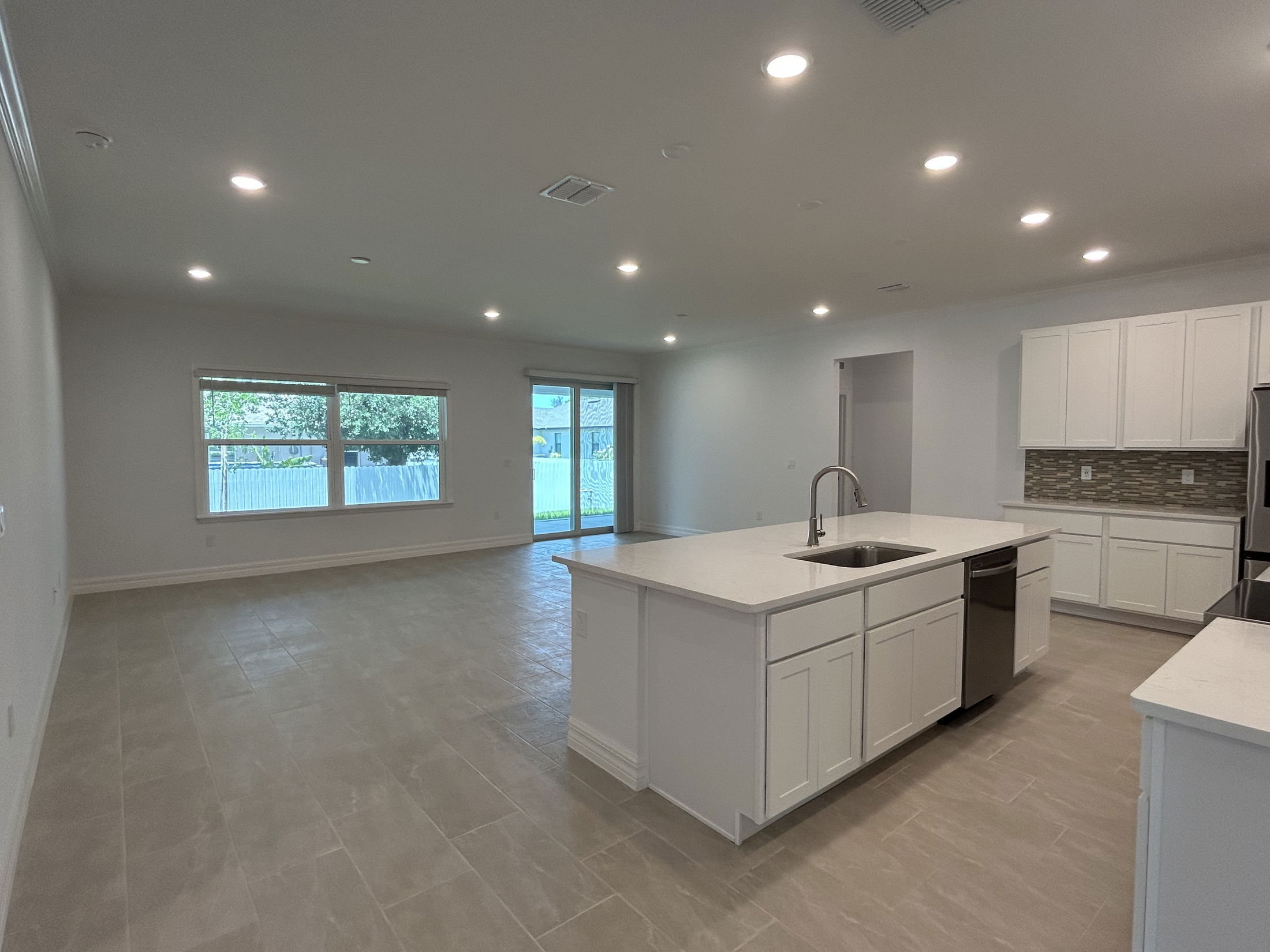 Spacious modern kitchen with white cabinetry, central island, and large windows overlooking a backyard.
