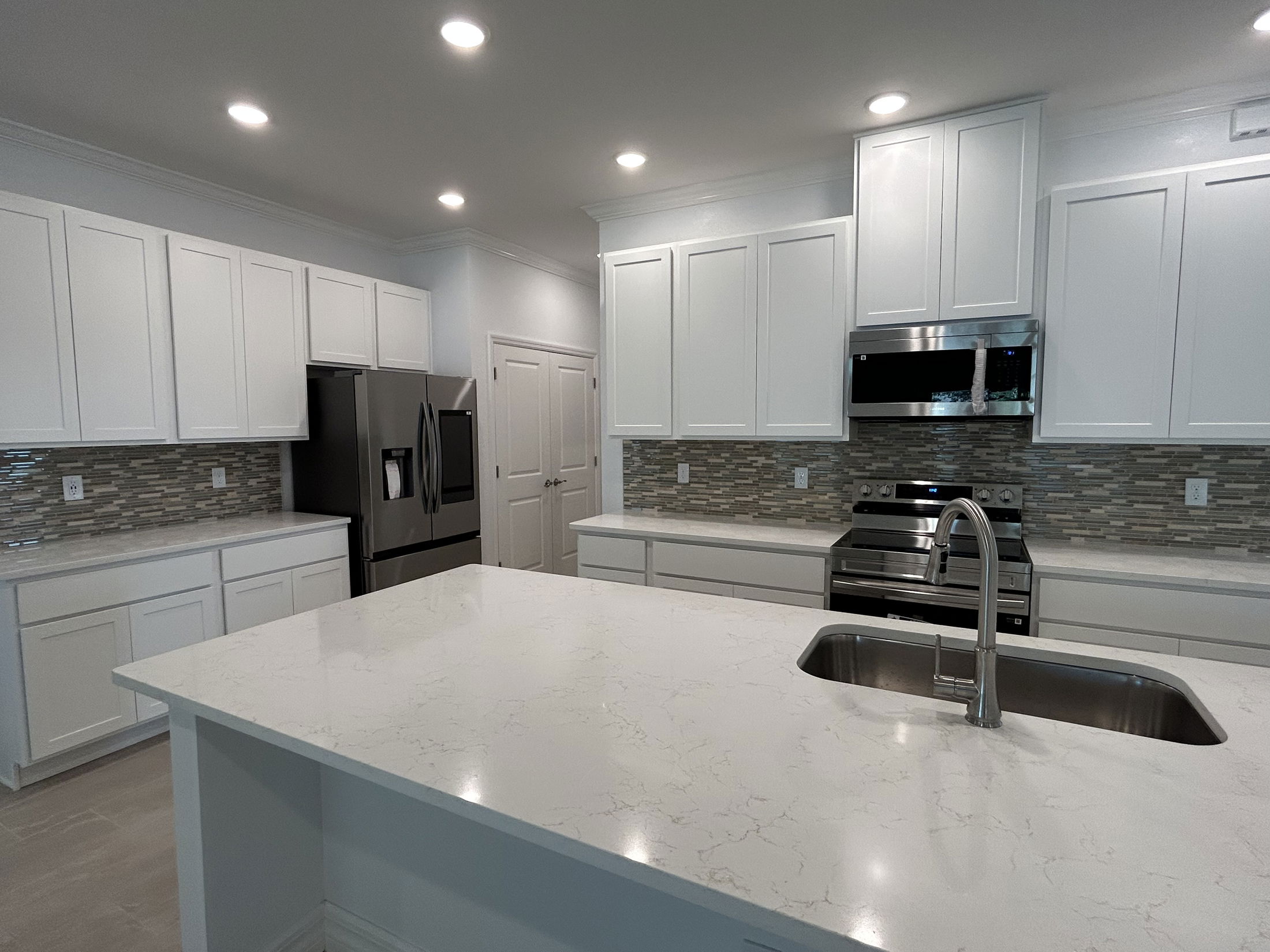 Modern kitchen with white cabinets, marble countertops, stainless steel appliances, and tile backsplash.