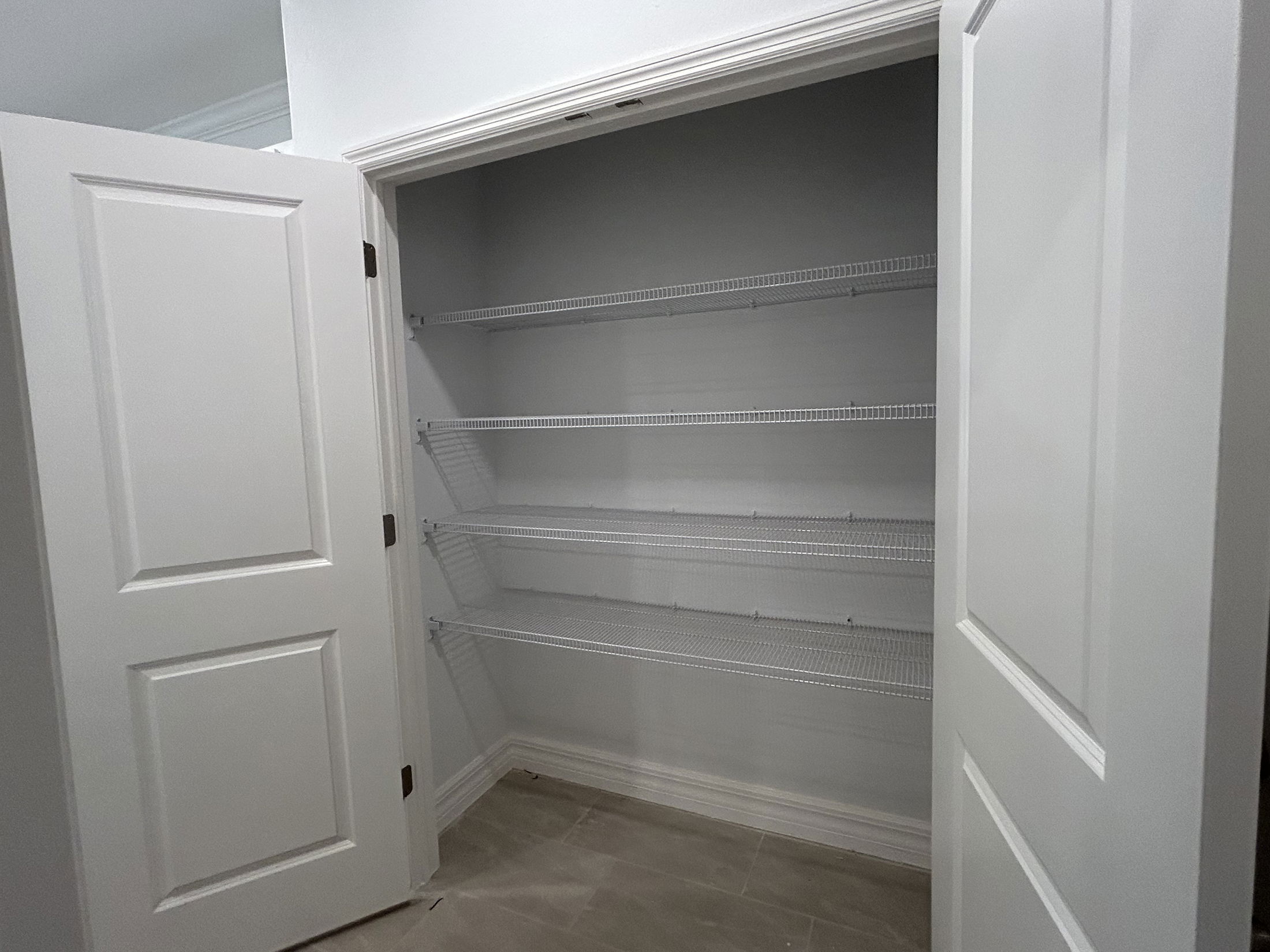 Empty white closet with open doors revealing wire shelves inside.