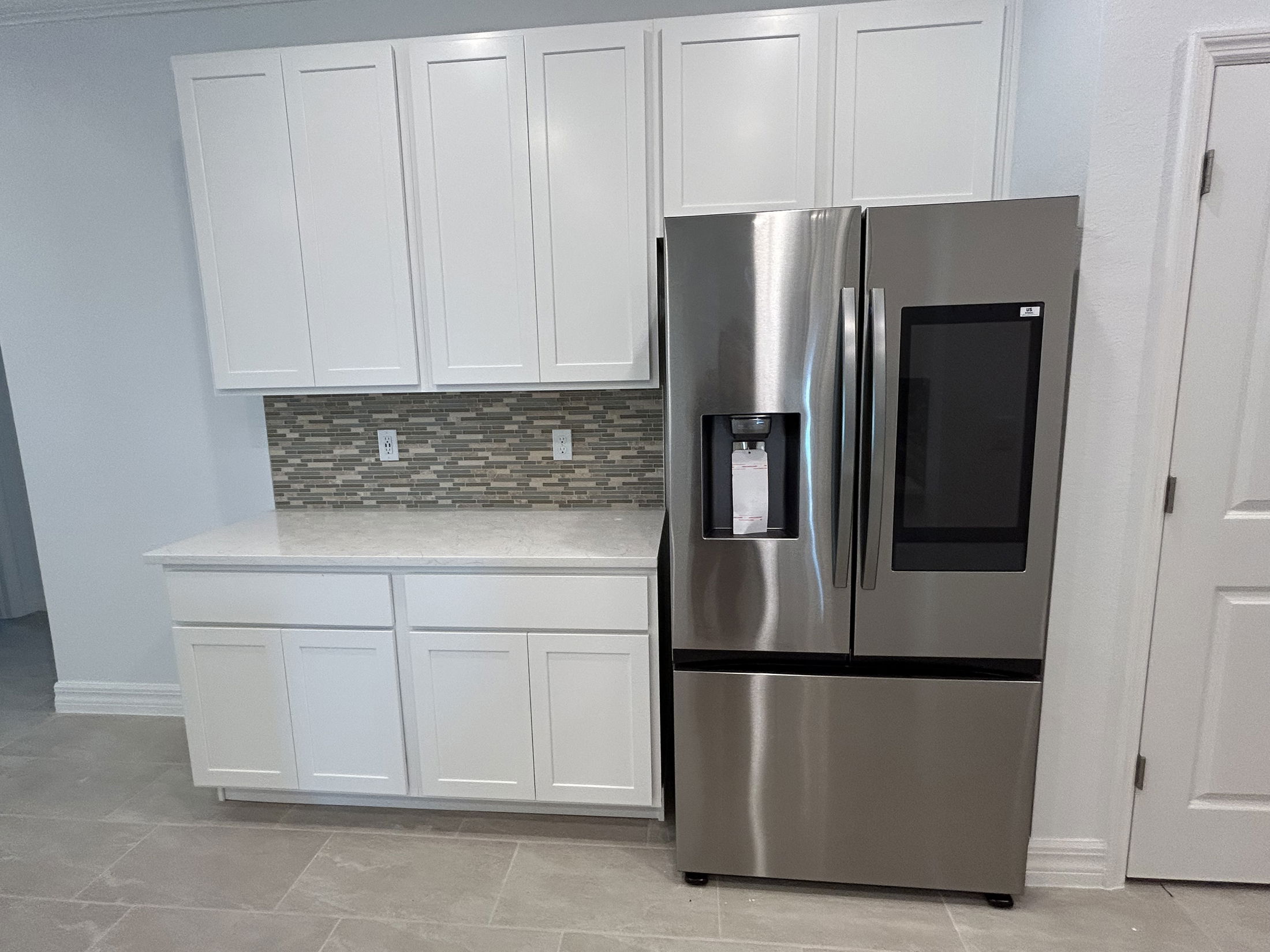 Modern kitchen with stainless steel refrigerator, white cabinets, and tiled backsplash.