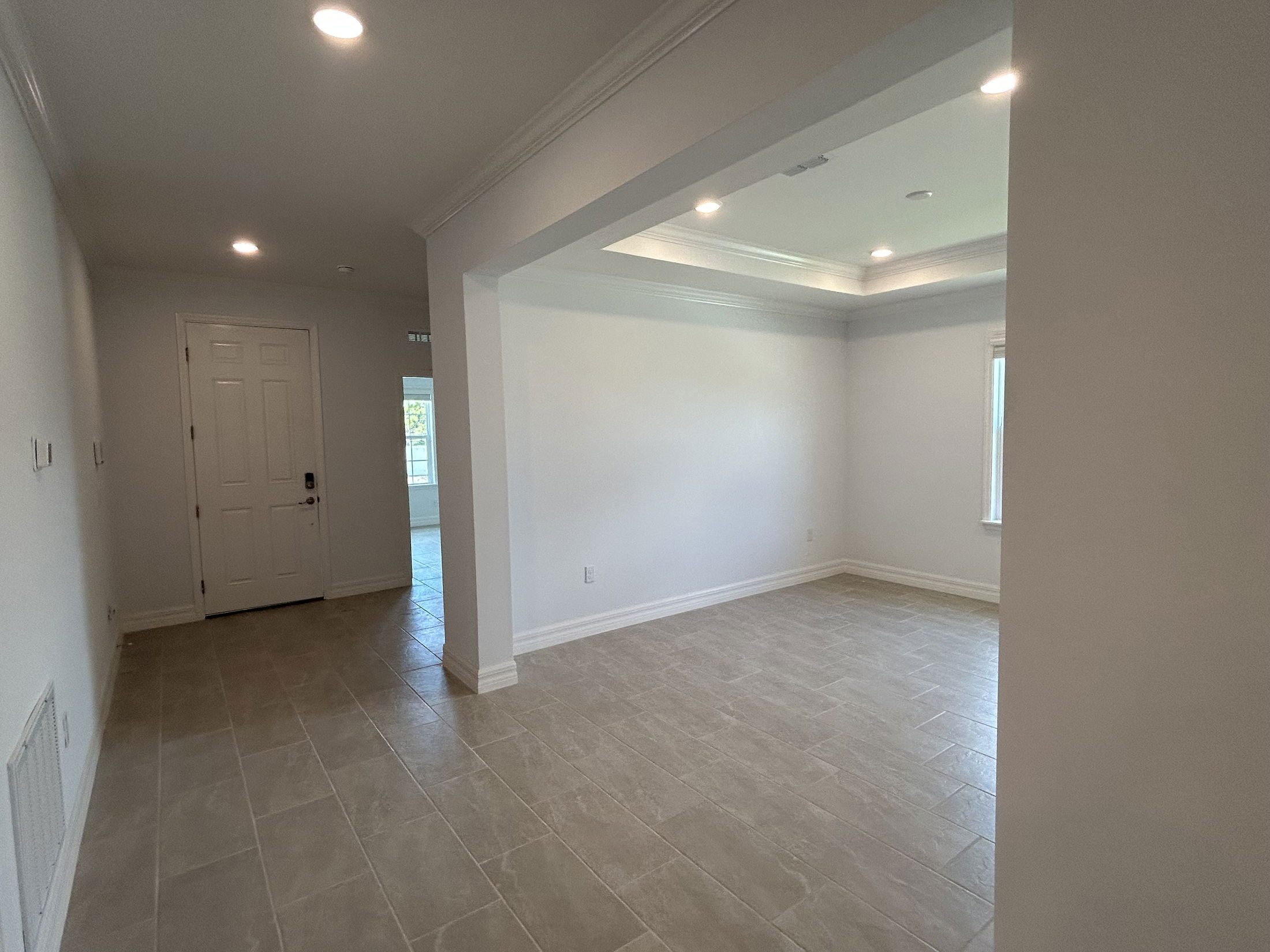 Modern, empty room with recessed lighting, light grey tiled floors, and a white front door.