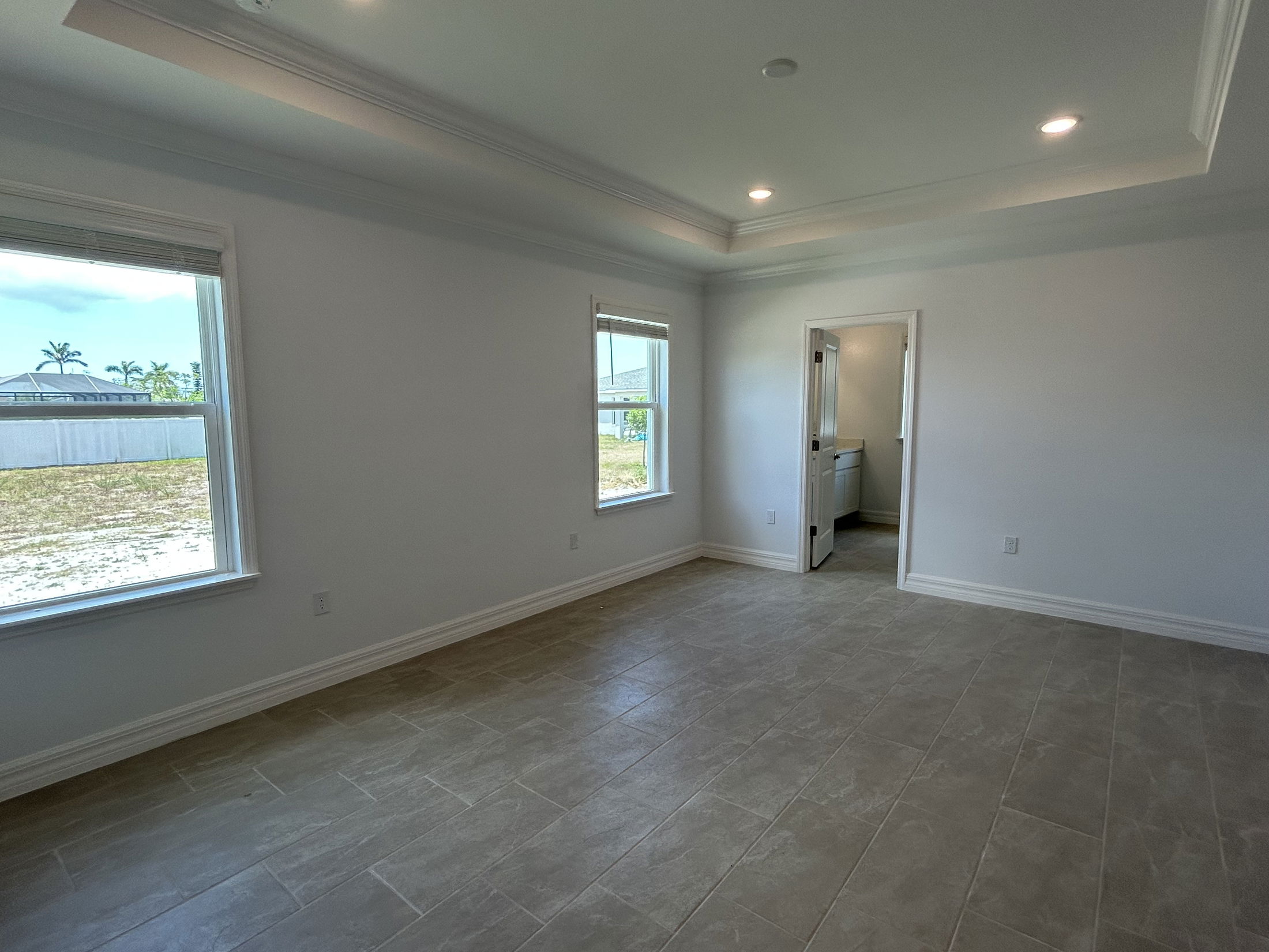 Modern empty room with tiled floors, recessed lighting, and large windows providing natural light.