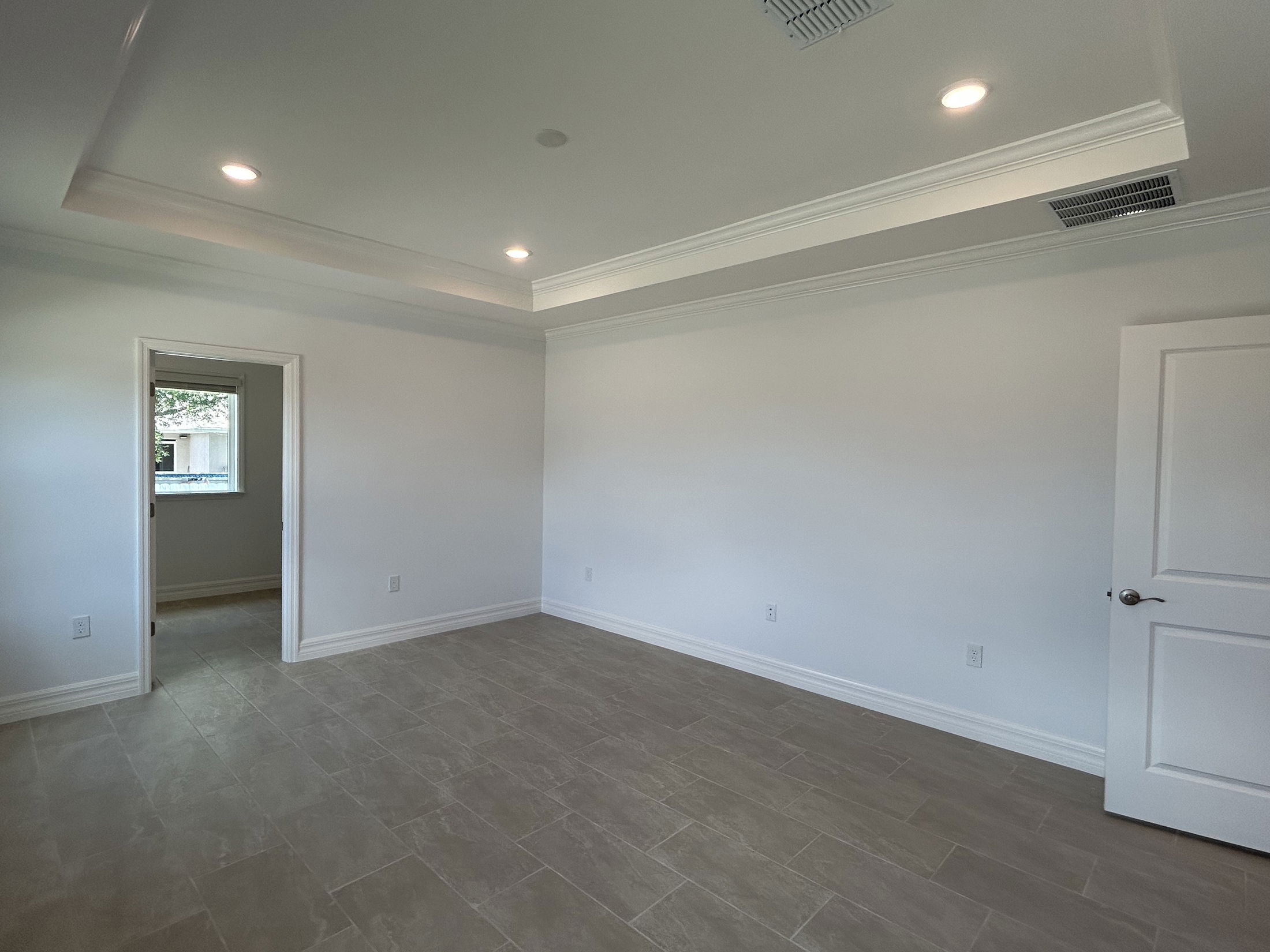 Empty room with recessed lighting, white walls, tiled flooring, and an open door leading to a windowed space.