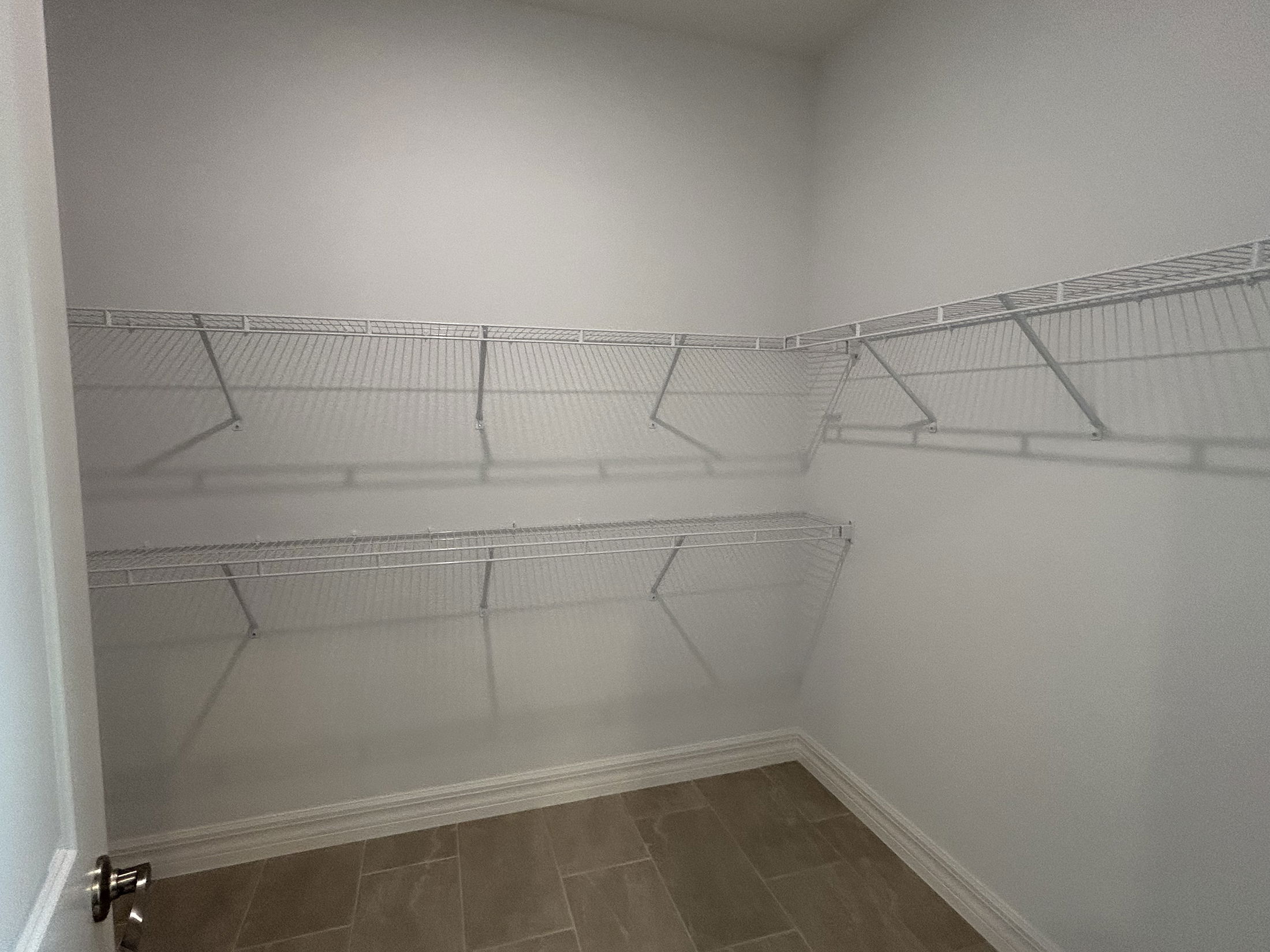 Empty walk-in closet with white wire shelving on grey tiled floor.