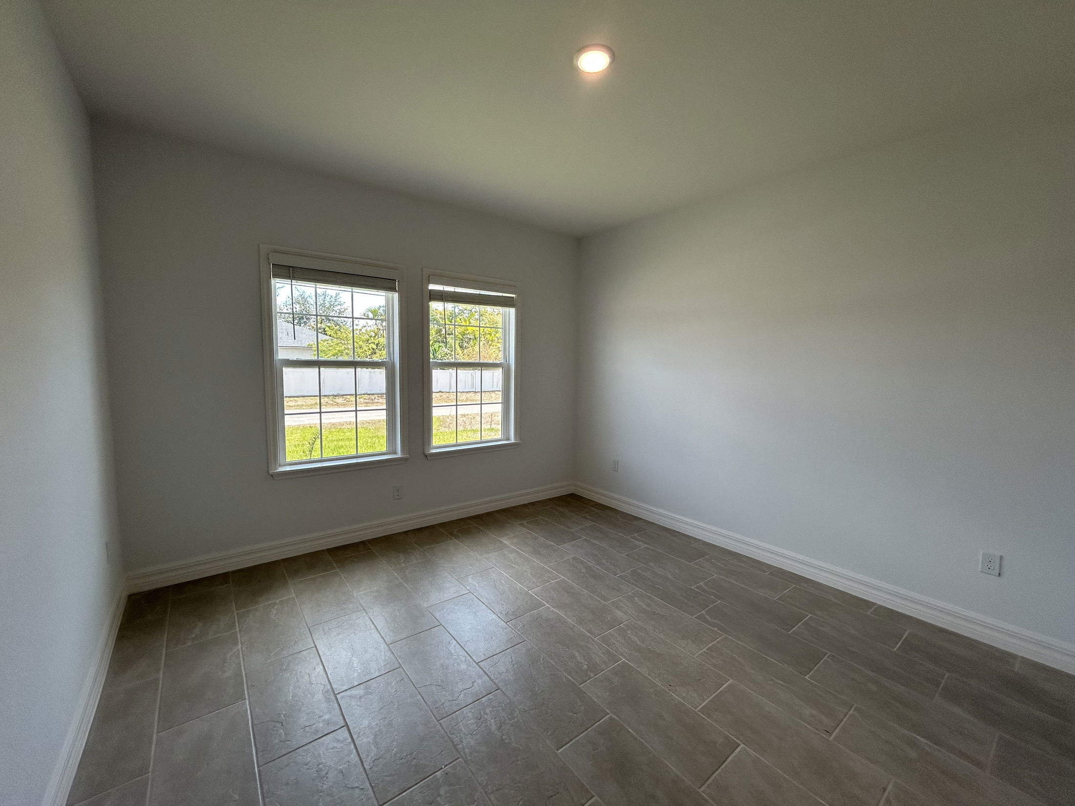 Bright empty room with large windows, light gray walls, and tiled floor.