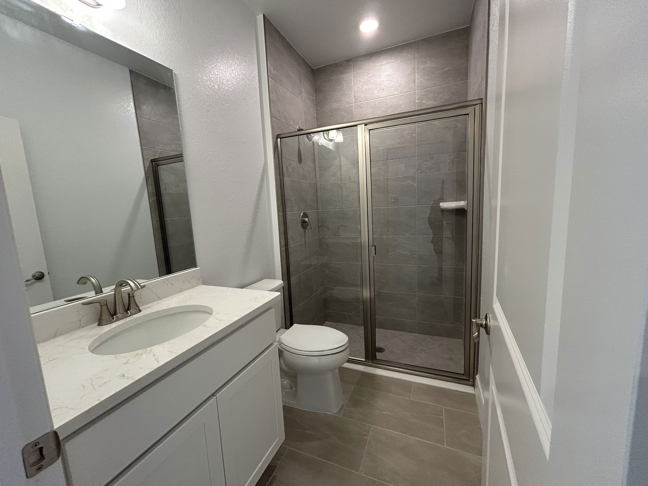 Modern bathroom featuring a glass-enclosed shower, white vanity with marble countertop, and tiled walls and floors.
