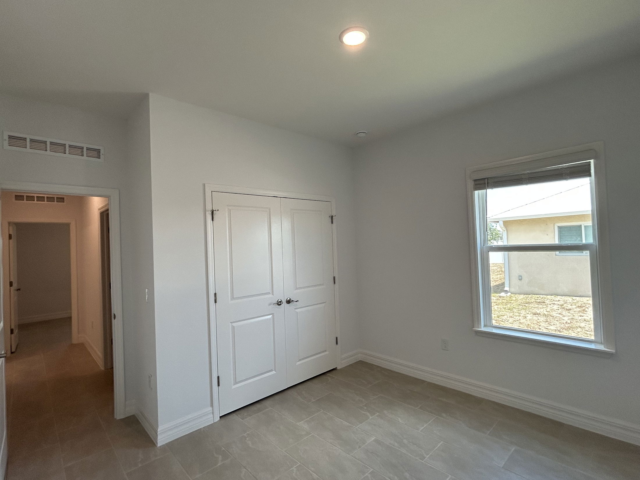 Empty white room with tile flooring, a double-door closet, and a window overlooking the exterior.