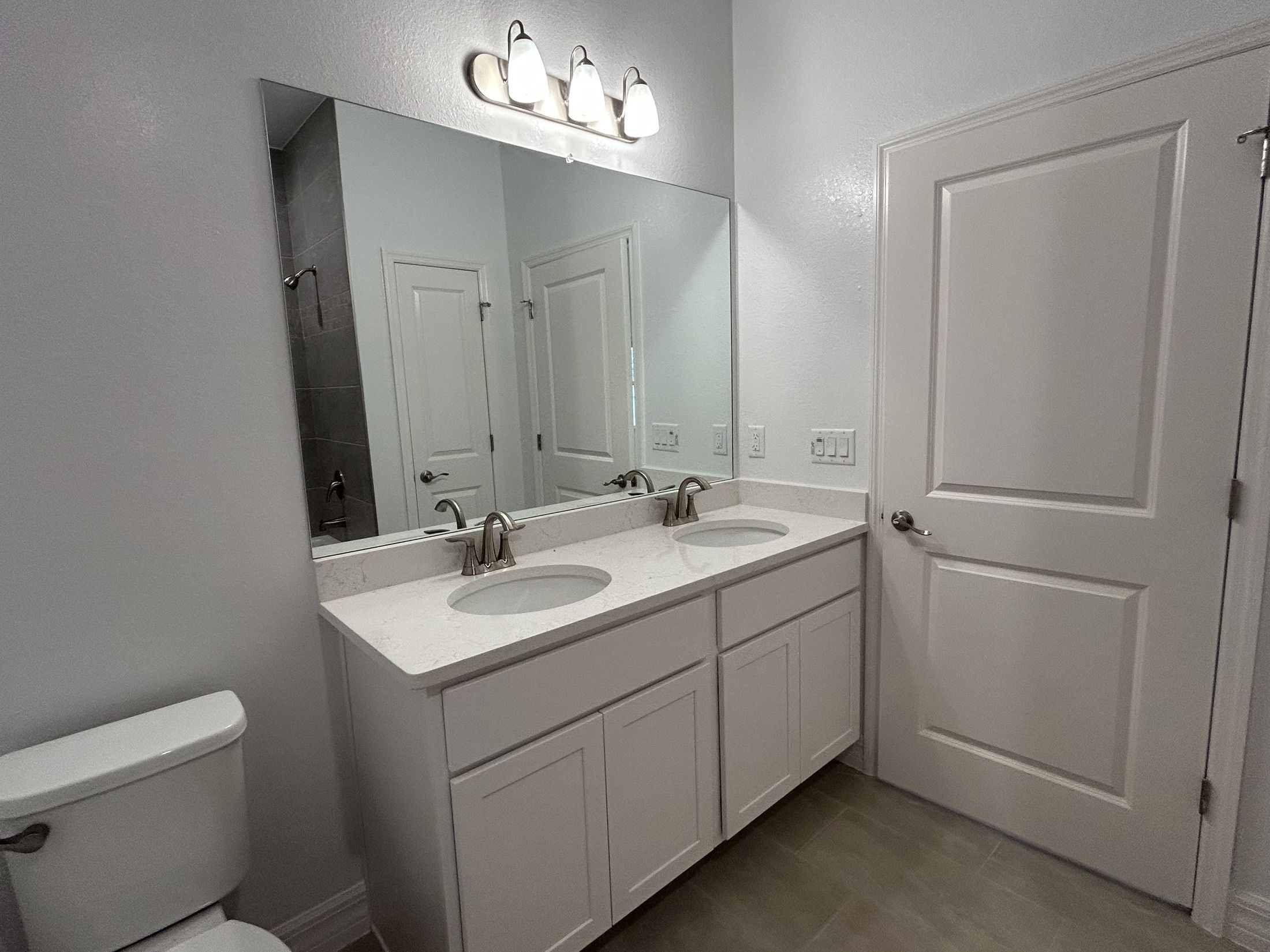 Modern bathroom with dual sinks, granite countertop, large mirror, and sleek lighting fixtures.