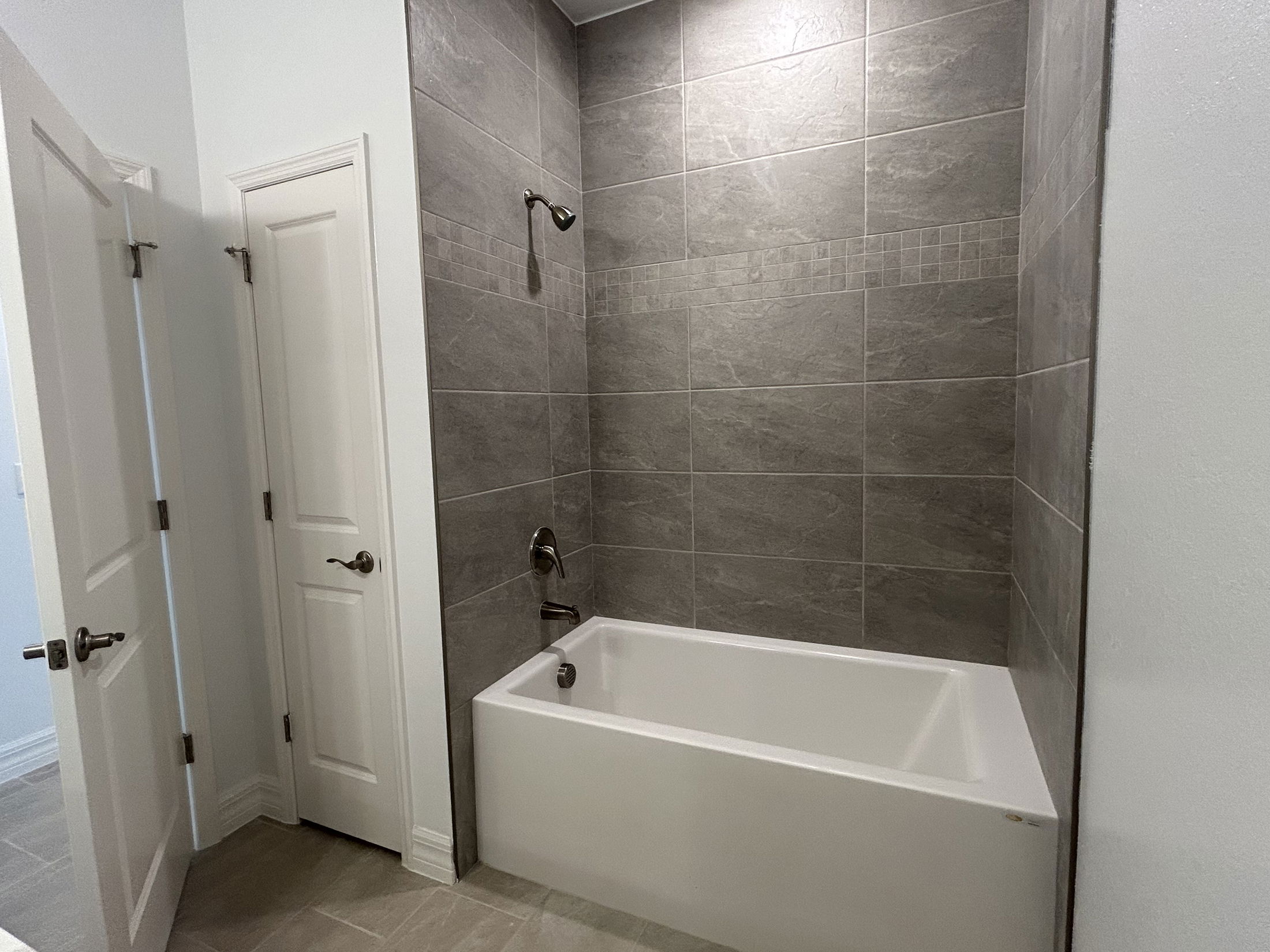 Modern bathroom with a white bathtub and gray tiled walls featuring a geometric accent.