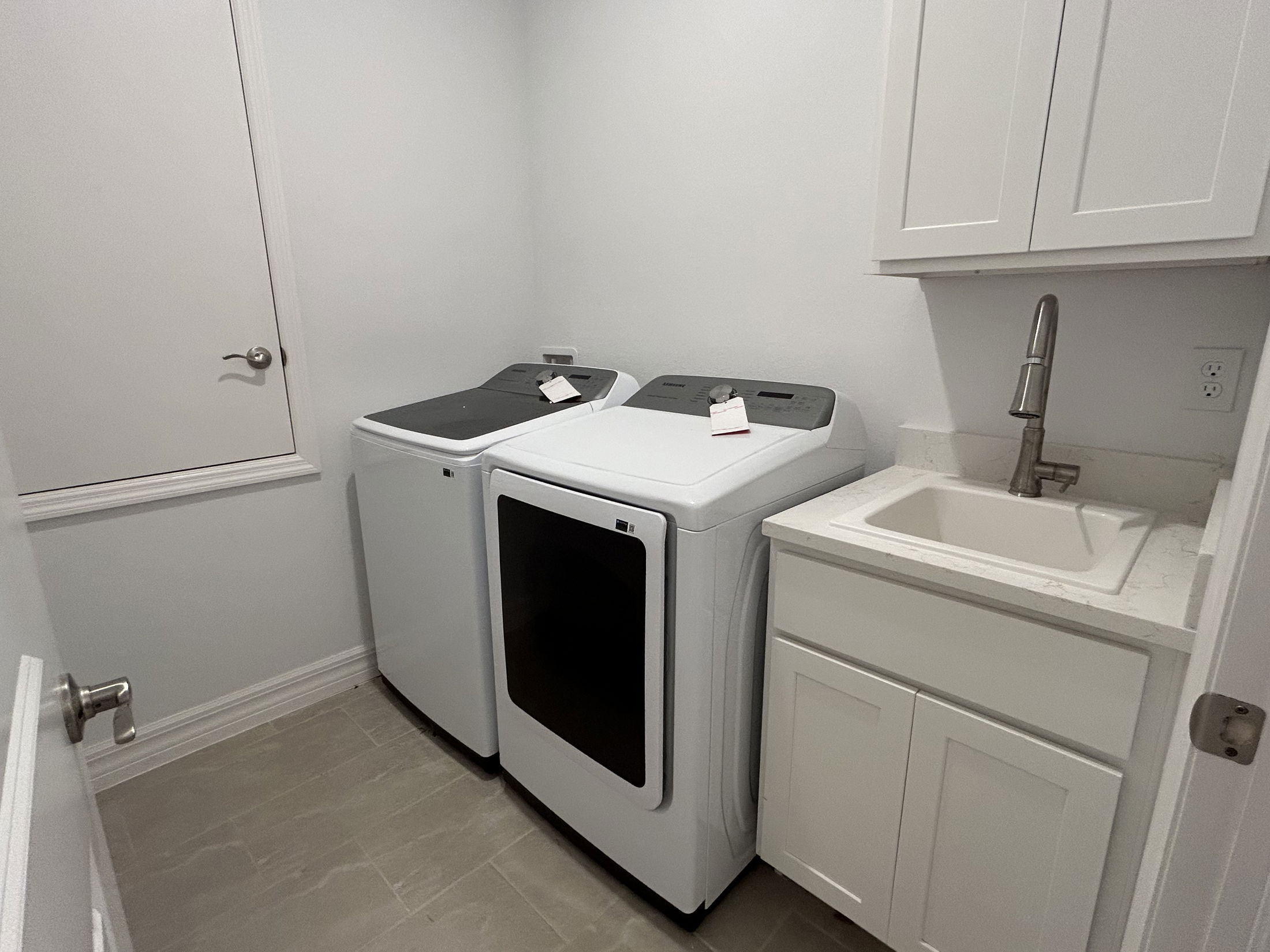 Modern laundry room with white cabinetry, a stainless steel sink, and a sleek washer and dryer set.