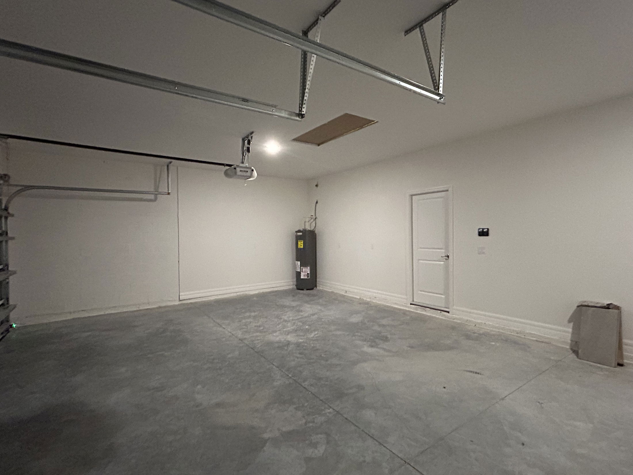 Empty residential garage with a concrete floor, water heater, and closed door.