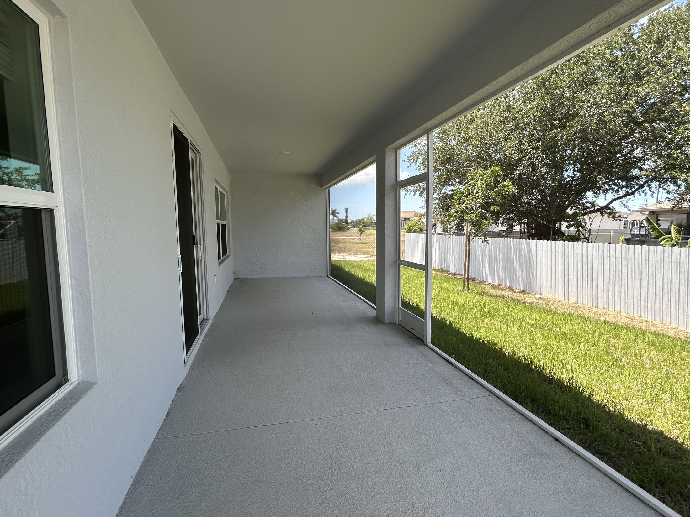 Covered patio with screened windows overlooking a grassy backyard and a white fence on a sunny day.