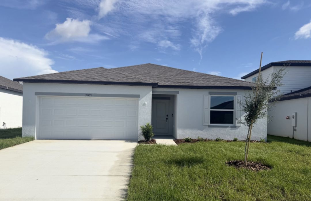 Single-story white house with a gray roof, a driveway, and green grass in the front yard.