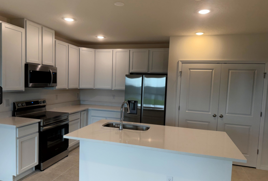 Modern kitchen with white cabinetry, stainless steel appliances, and a central island with a sink.
