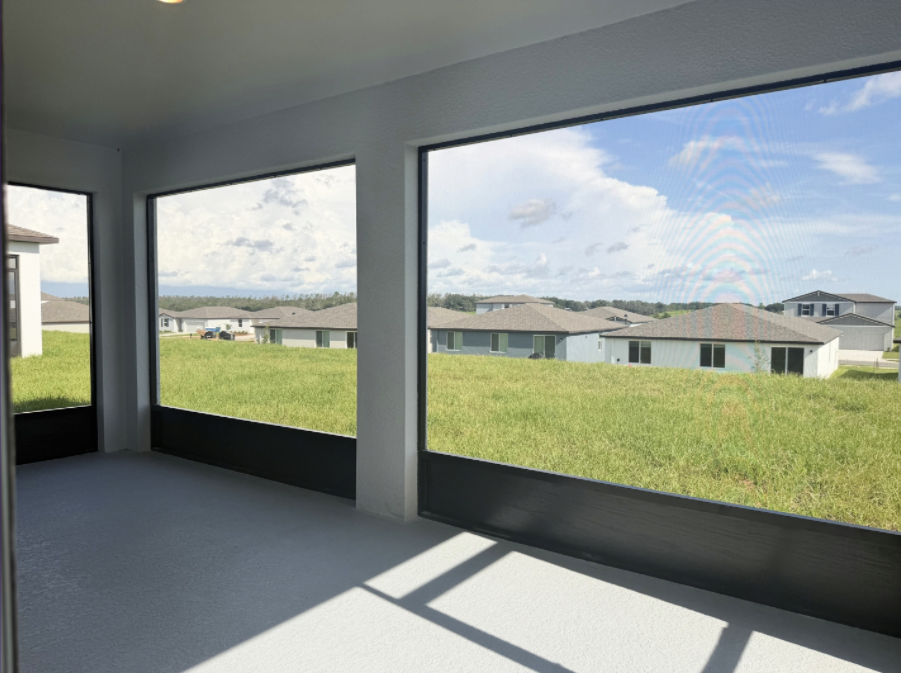 View of a grassy landscape and houses through large windows in a screened porch.