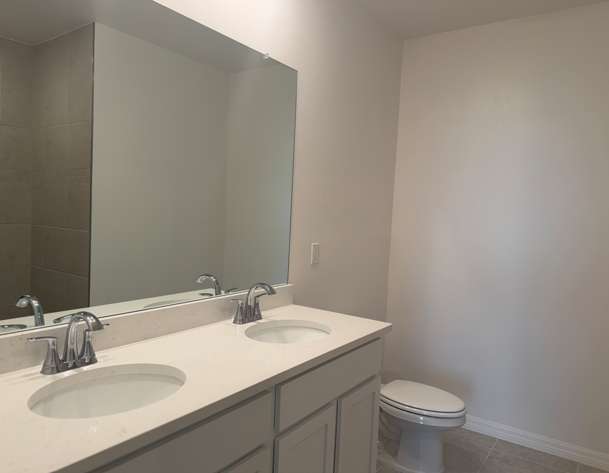 A modern bathroom featuring a double sink vanity with a large mirror, beige tiled walls, and a white toilet.