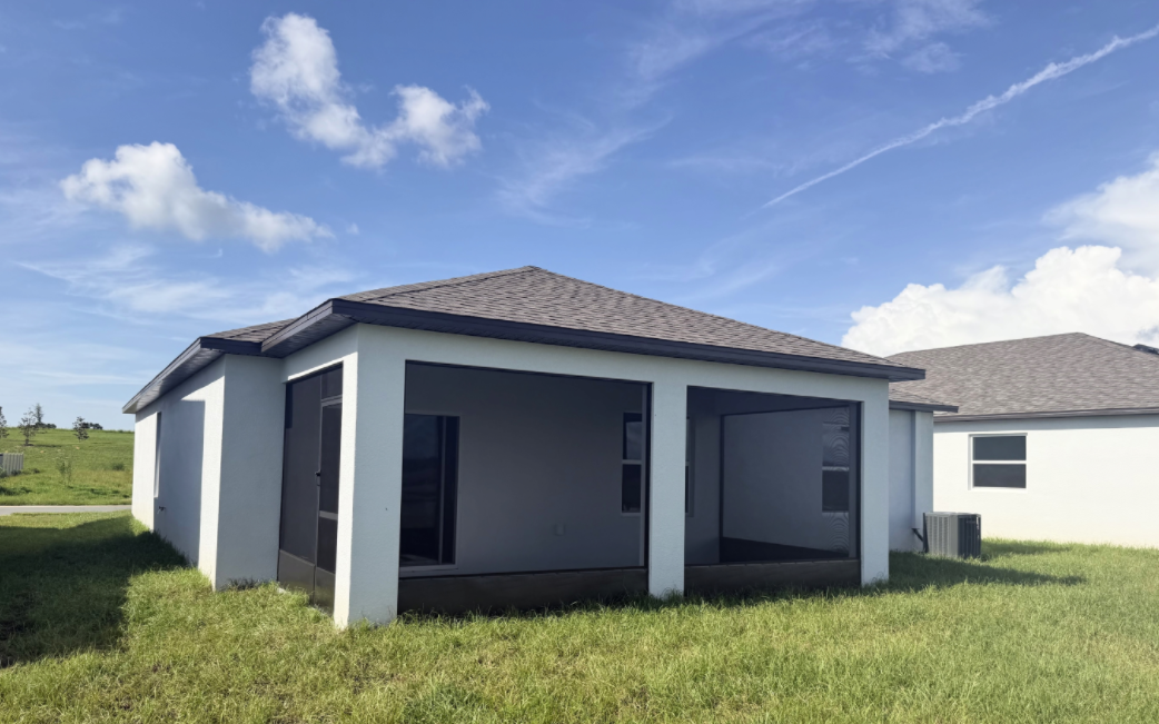 A single-story house with a sloped roof and screened porch set against a blue sky and grassy landscape.