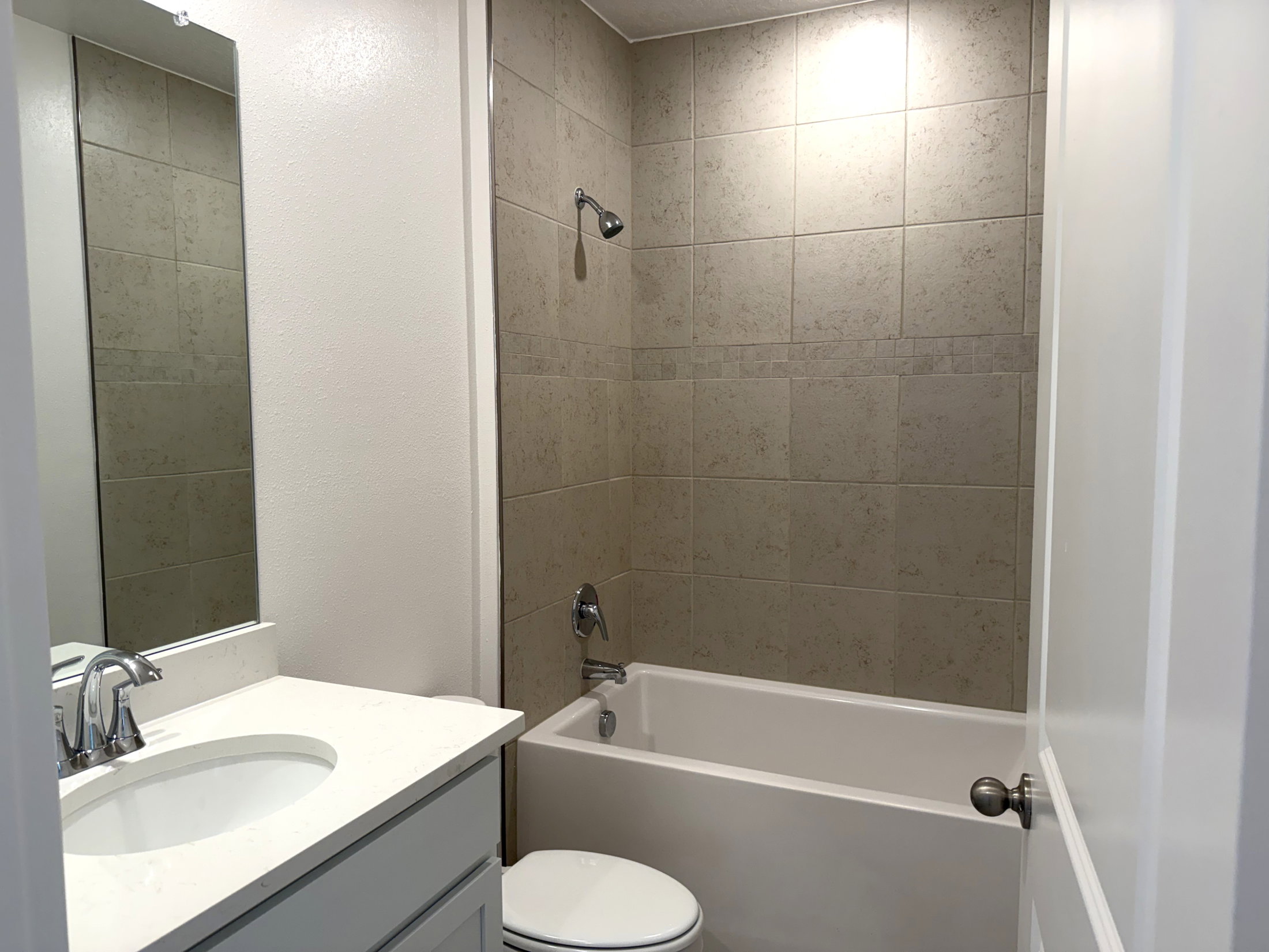 A small bathroom featuring a bathtub, a showerhead, and a sink with a mirror above it.