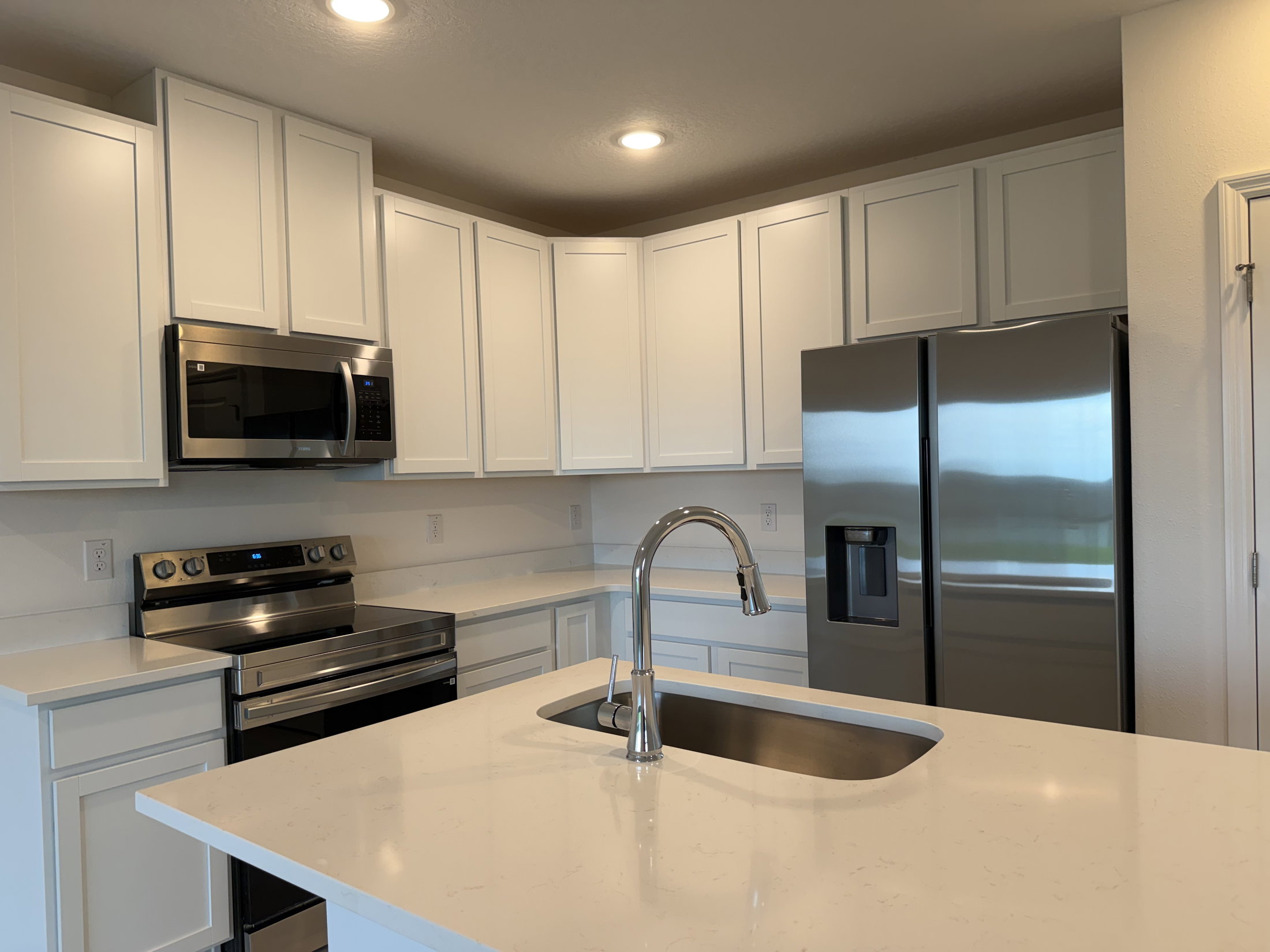 Modern kitchen featuring white cabinetry, stainless steel appliances, and a large countertop island with a sink.