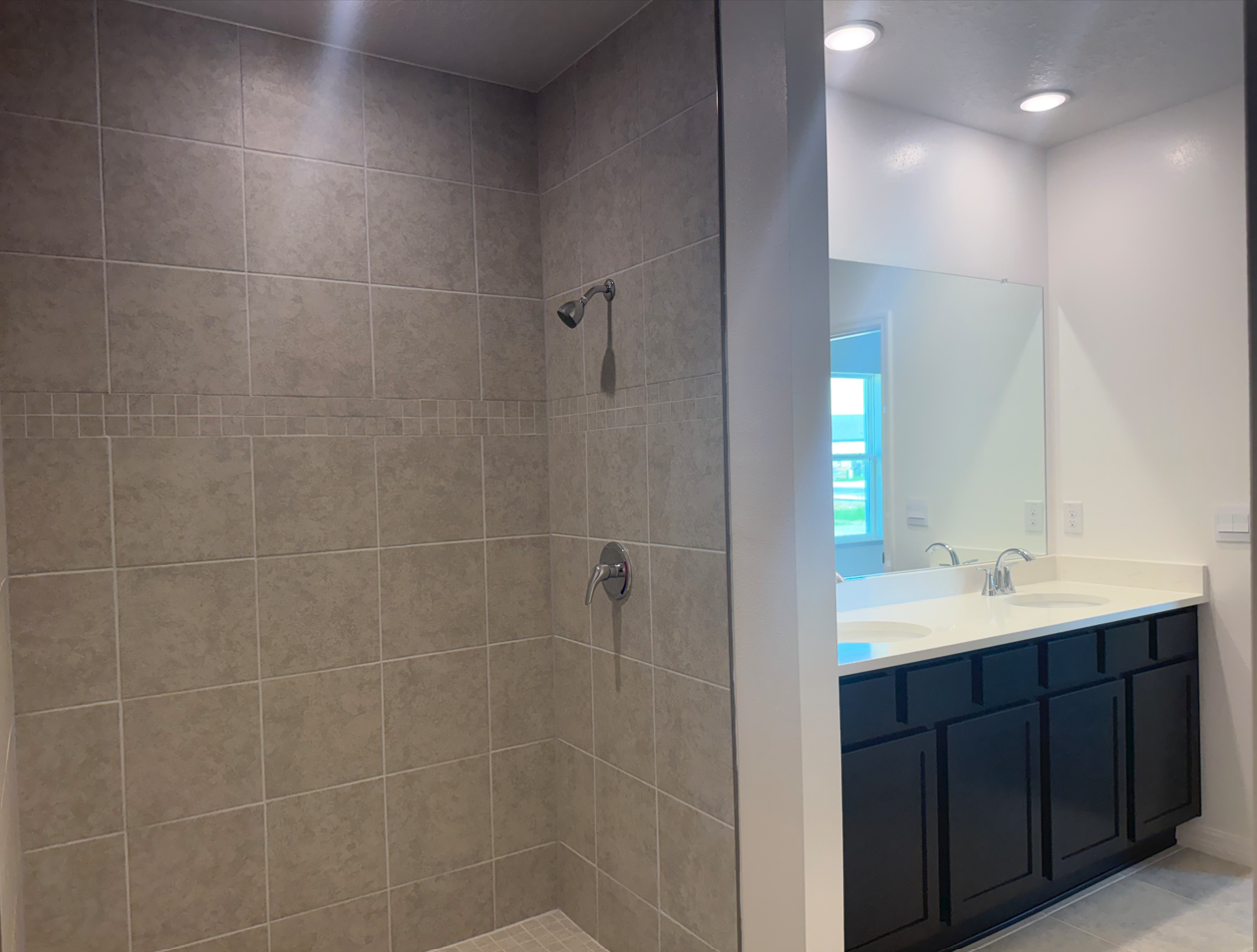 A modern bathroom featuring a tiled shower on the left and a double-sink vanity with dark cabinets on the right.