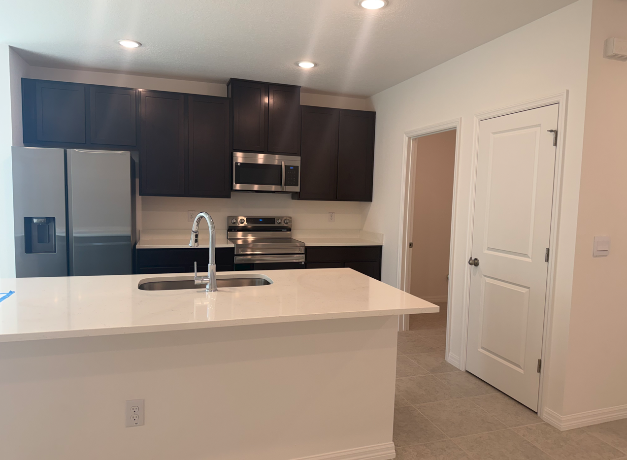Modern kitchen featuring dark cabinets, stainless steel appliances, and a large island with a sink.