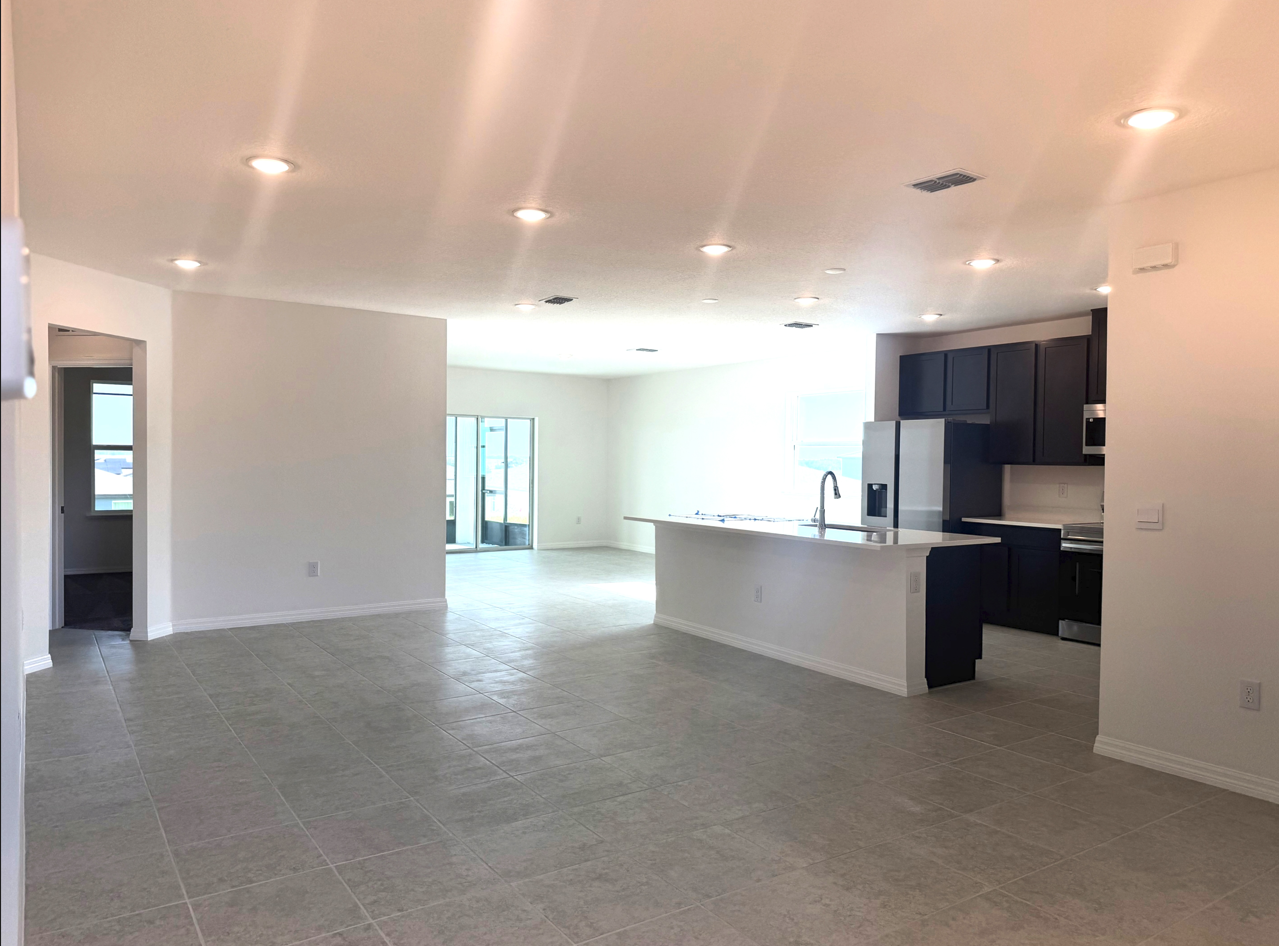 Spacious, modern living area featuring tile flooring, recessed lighting, and an open kitchen.