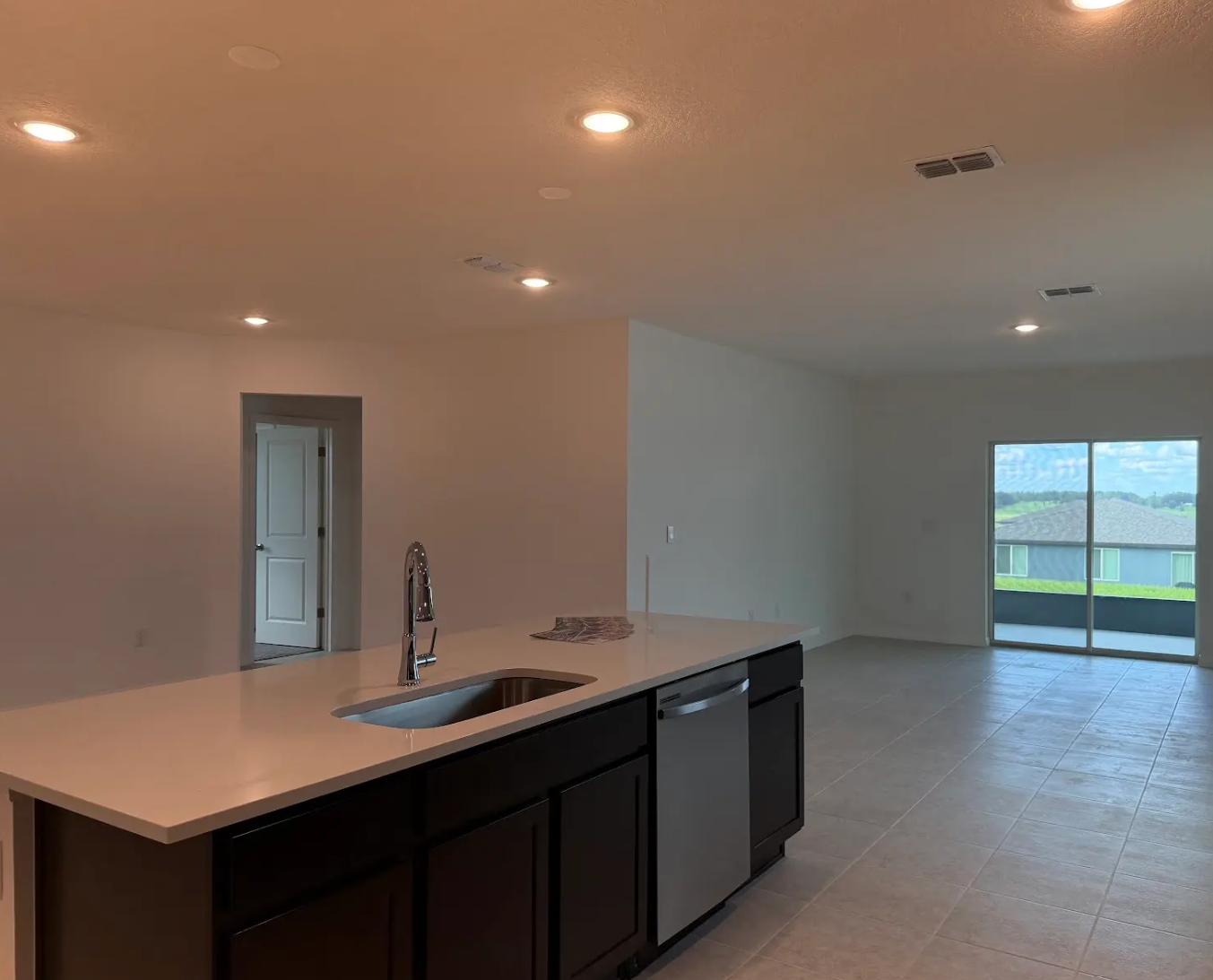 Modern kitchen with a central island, stainless steel dishwasher, and an open living area featuring large sliding glass doors leading to a balcony.