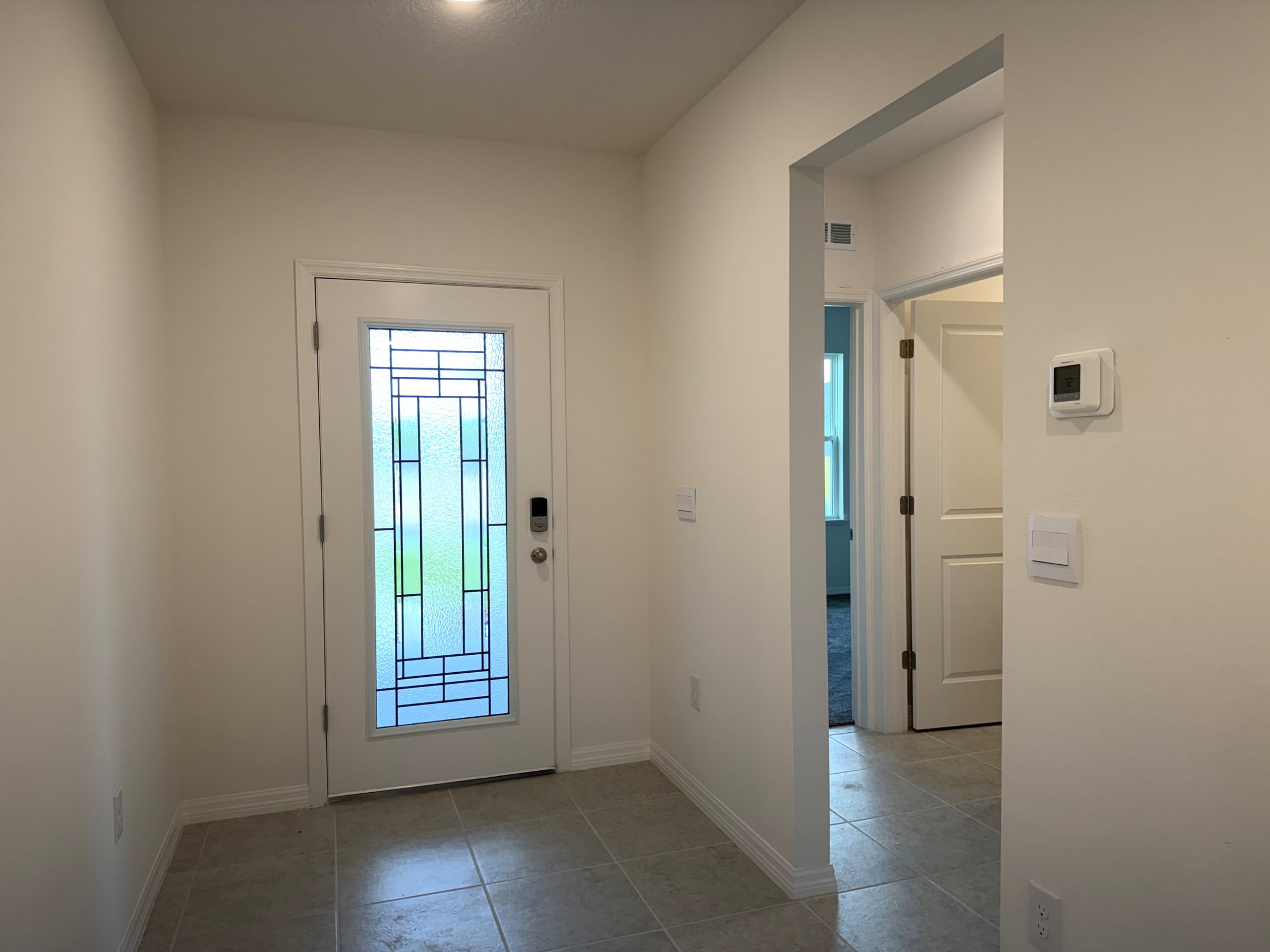 Bright entryway with a decorative glass door, light-colored walls, and tiled floor.
