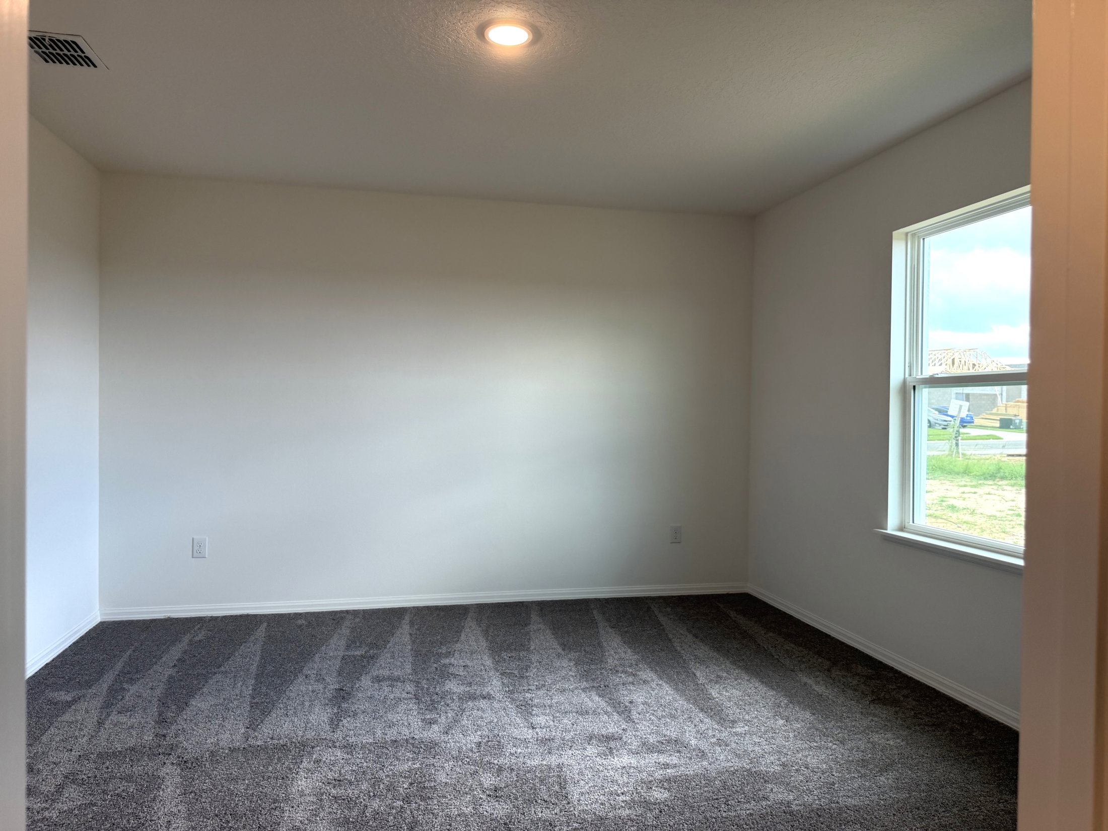 Empty room with gray carpet and a window letting in natural light.