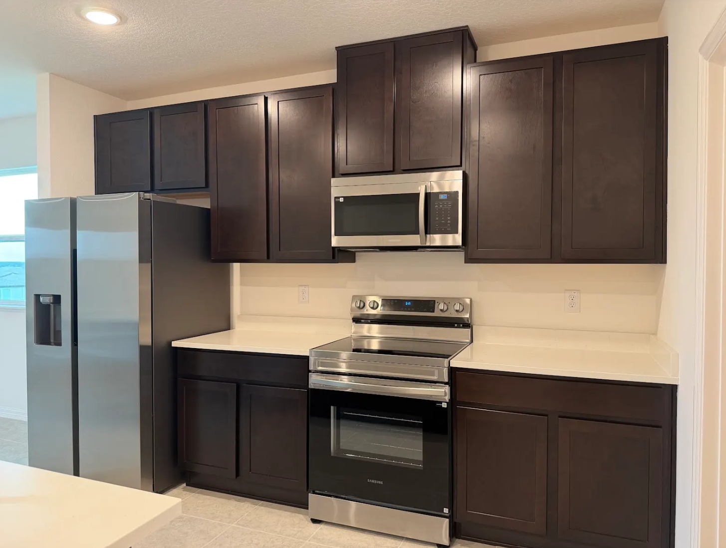 Modern kitchen featuring dark wood cabinets, stainless steel appliances, and a light countertop.